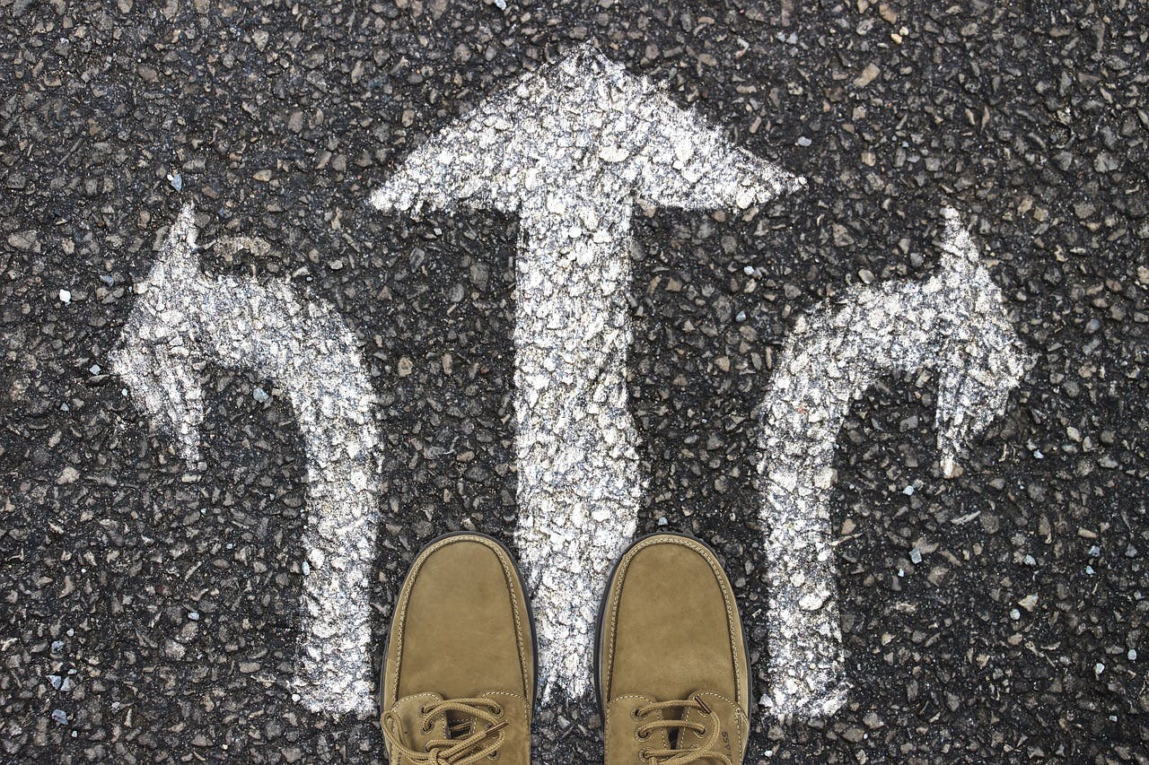 A person stands on a road, with two arrows pointing in different directions. The image represents the choice of the right transport option from Barcelona to Salou.