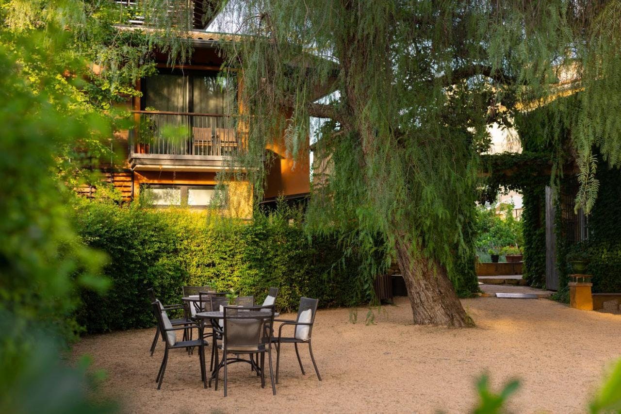 A charming patio at La Boella, a romantic hotel, featuring a table and chairs set against a backdrop of a beautiful tree.