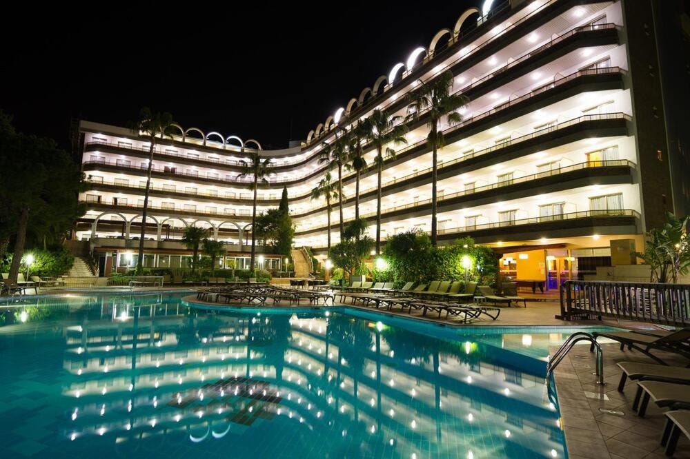 A night view of Golden Port Salou & Spa, a resort hotel, featuring an outdoor pool and lounge chairs for an evening of relax.