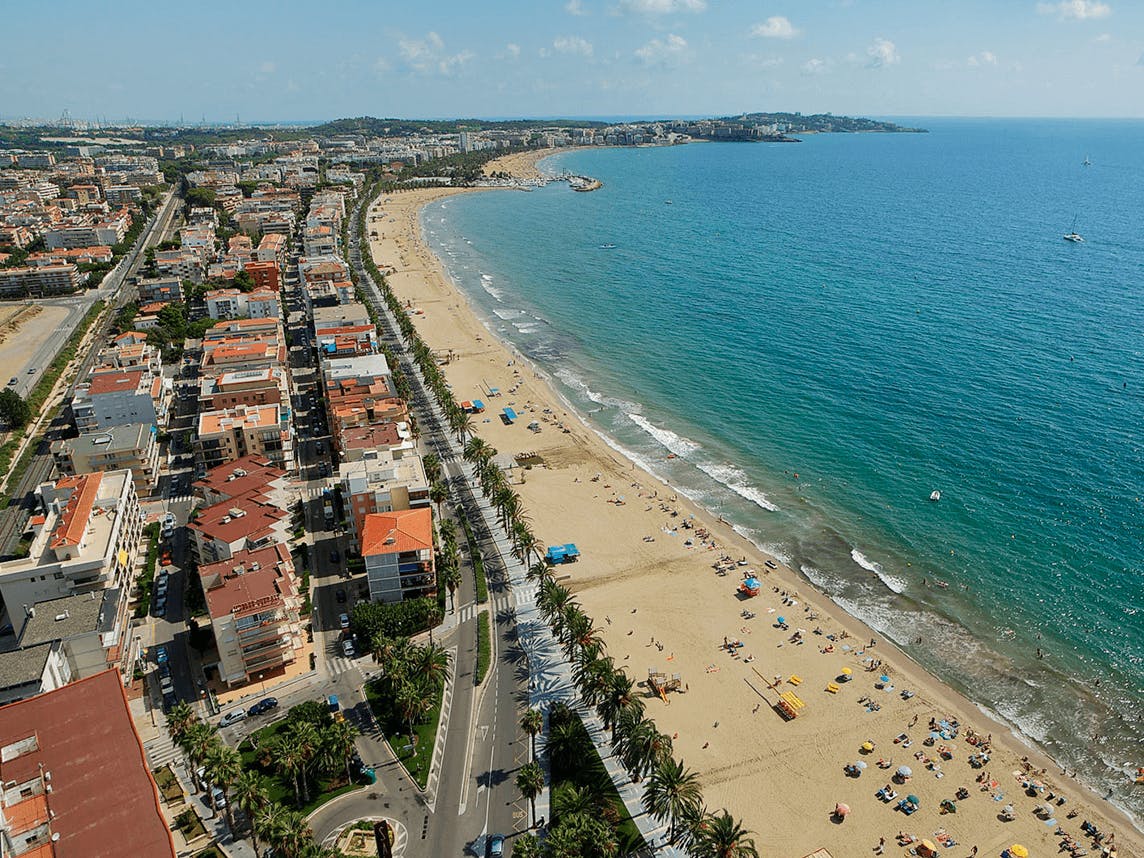 A bustling Ponent Beach, filled with people and buildings, offers a vibrant seaside scene.