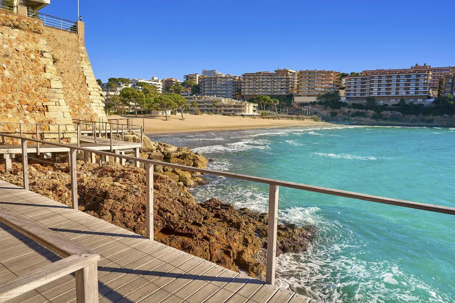 A scenic wooden walkway leading to the beach and ocean along the Camí de Ronda, a coastal path.