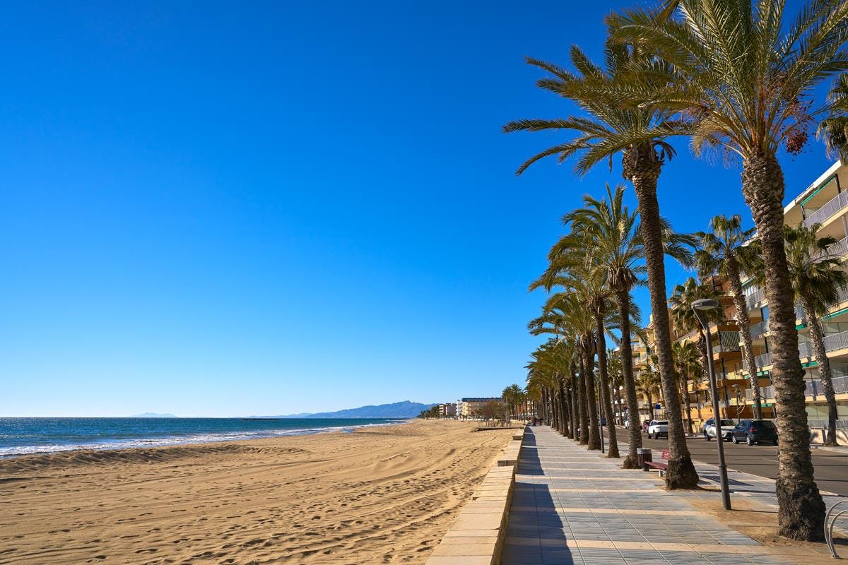 Playa de Ponent, Salou: A beautiful sandy beach with clear blue waters and palm trees lining the shore.