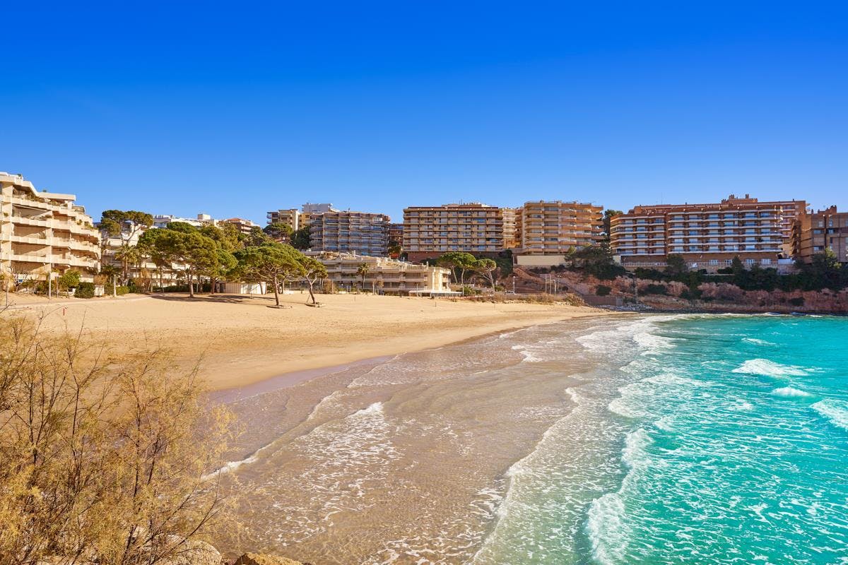 A stunning beach view of Capellans Beach, Salou, featuring a group of building overlooking the crystal-clear blue ocean.