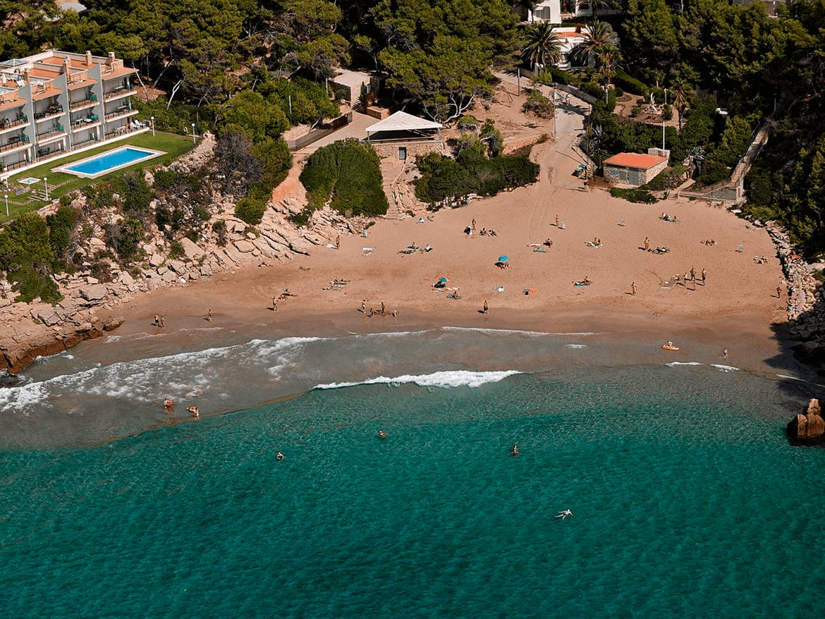 A picturesque beach at Cala Crancs, Salou, featuring a house and people enjoying a swim.