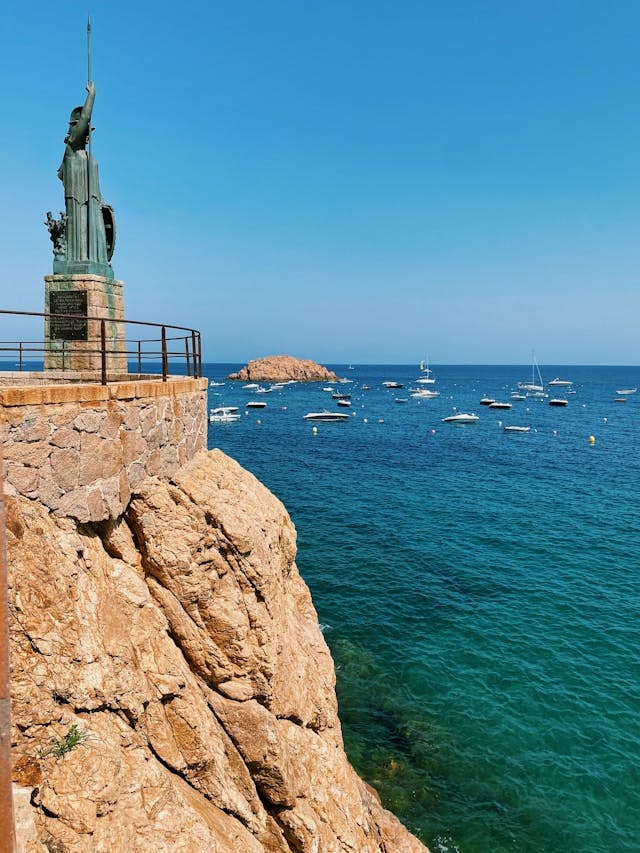 Une statue d'homme perchée sur un rocher, regardant le vaste océan devant elle.