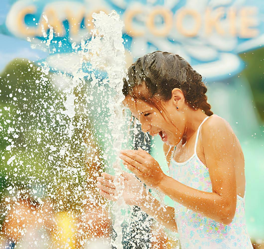 A young girl joyfully splashing water on her face outdoors.