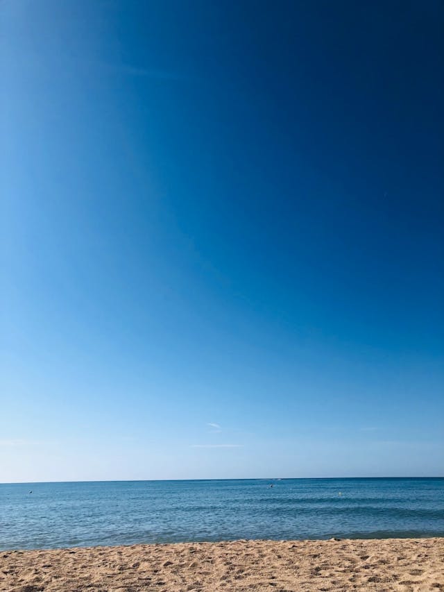 A sandy beach with a blue ocean and sky in the background.