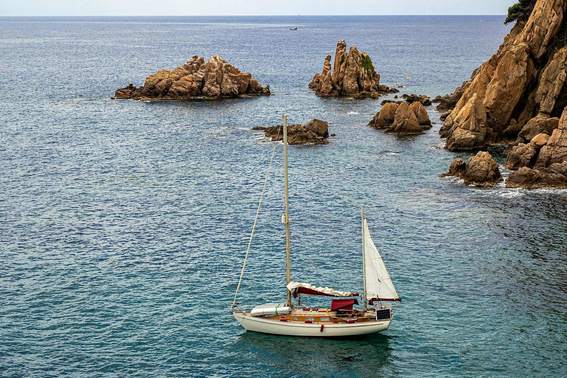 A sailboat in the ocean with rocks in the background.