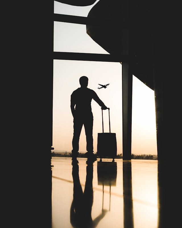 Un viajero con equipaje frente a un aeropuerto, listo para su viaje.
