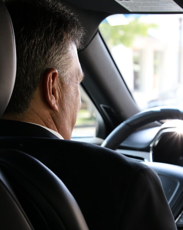 Un hombre conduciendo un coche con una mano en el volante, concentrado en la carretera.