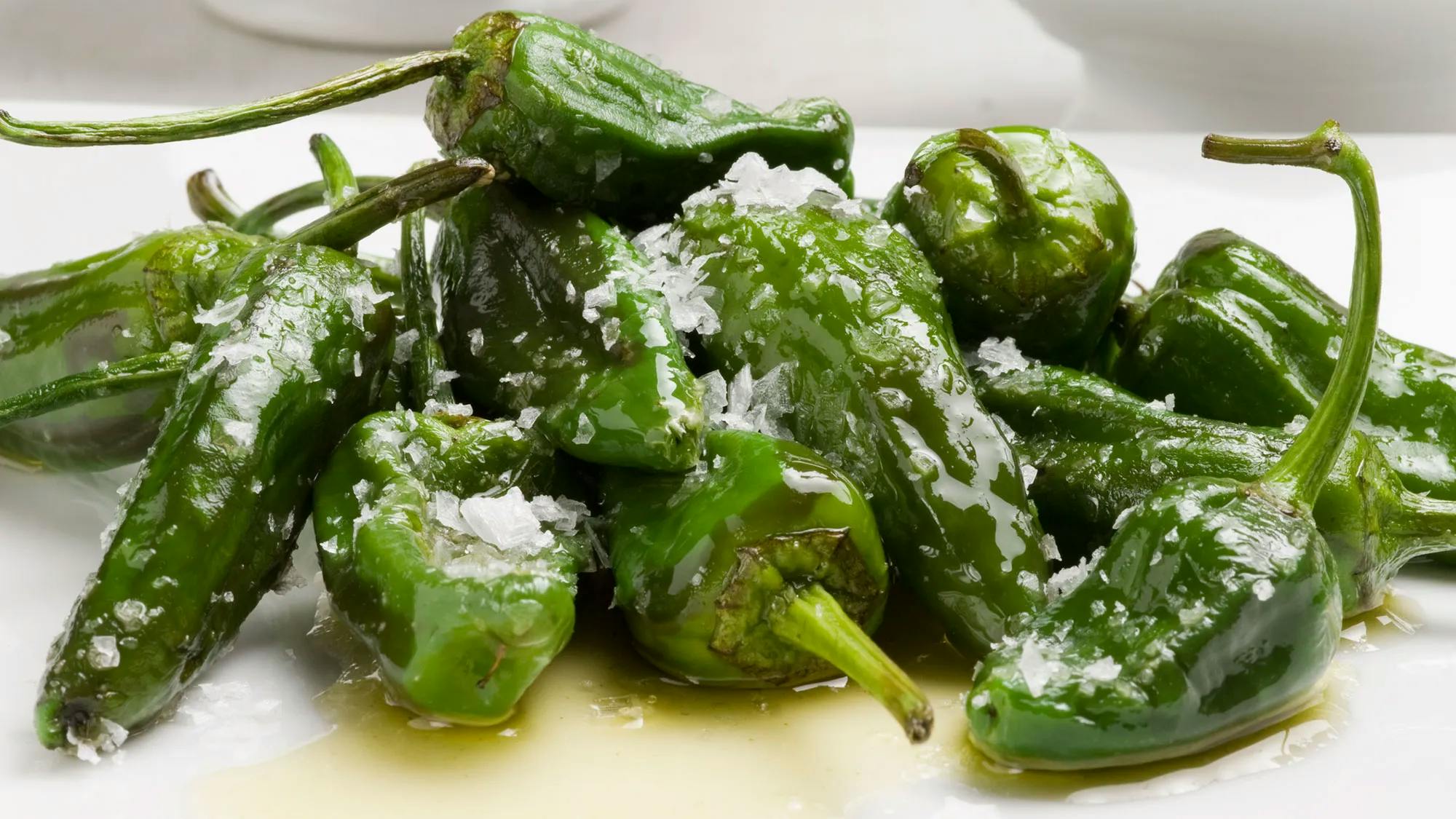 A plate of Pimientos al padrón, placed on a wooden table.