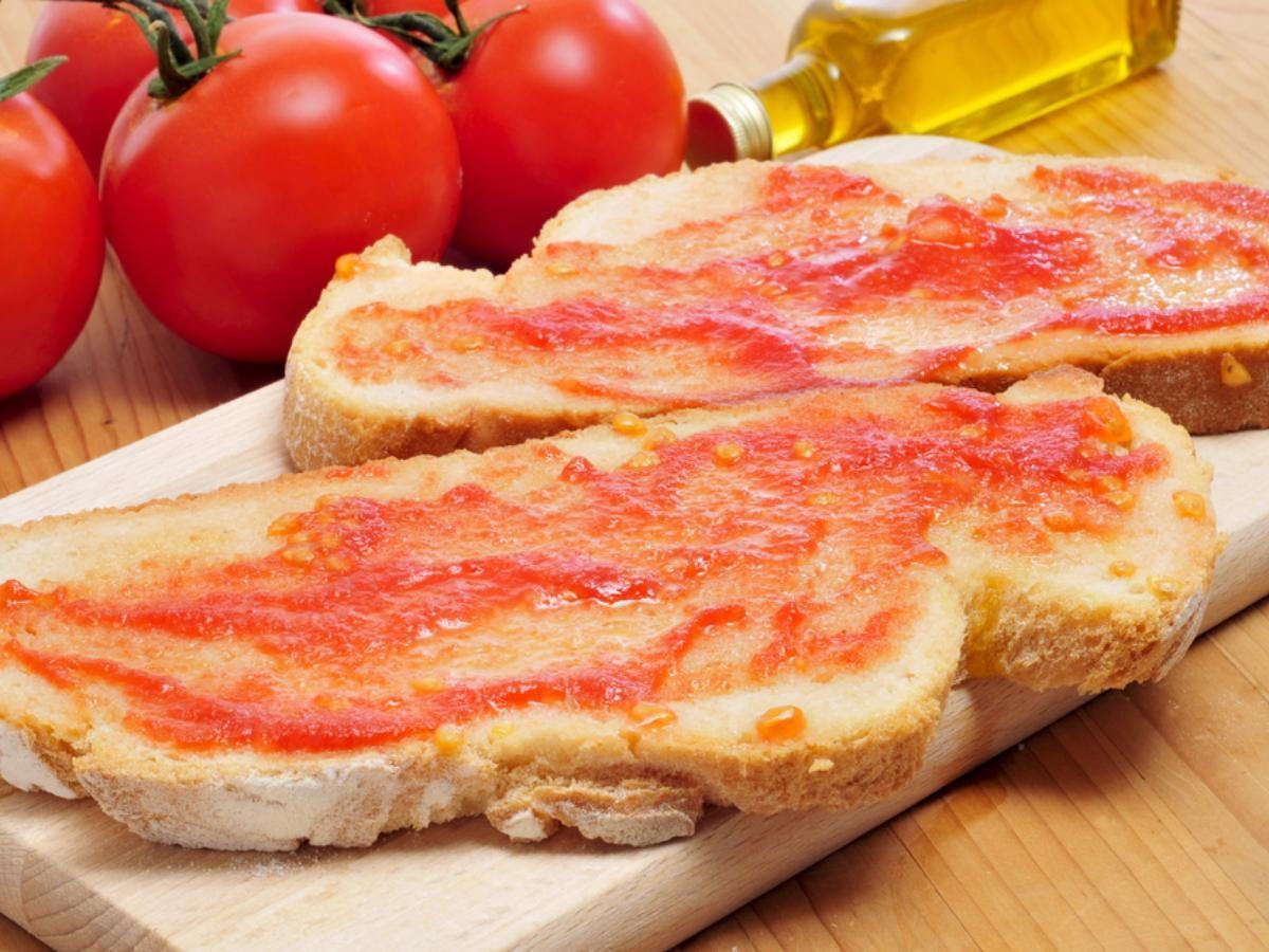 A wooden cutting board with two slices of bread, showcasing pan con tomate with fresh tomatoes.