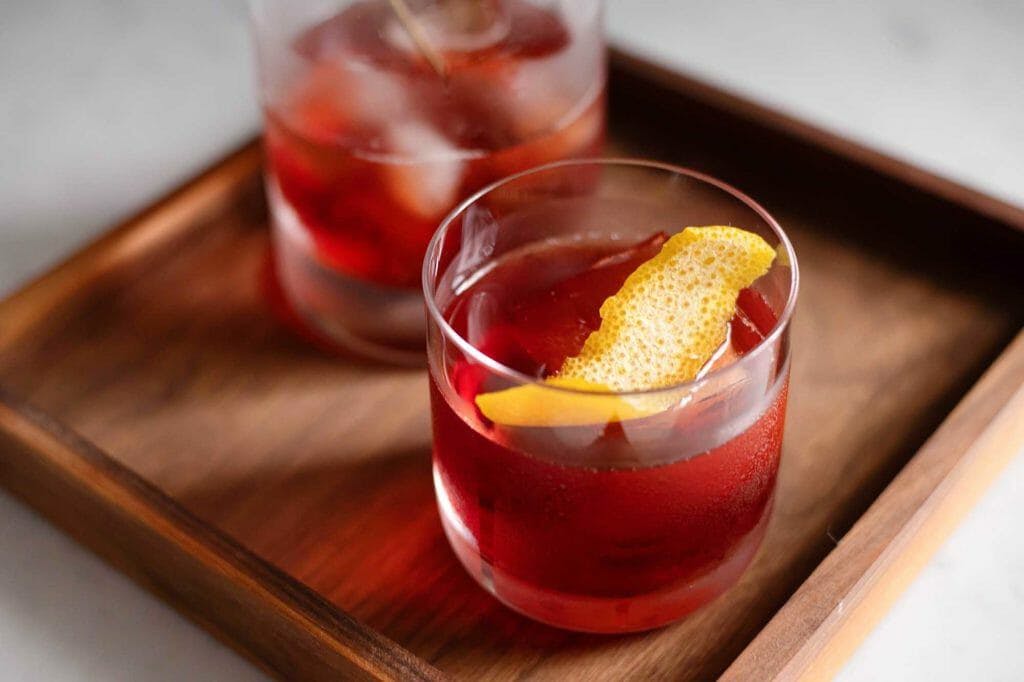 Two glasses of Vermouth rosso on a wooden tray.