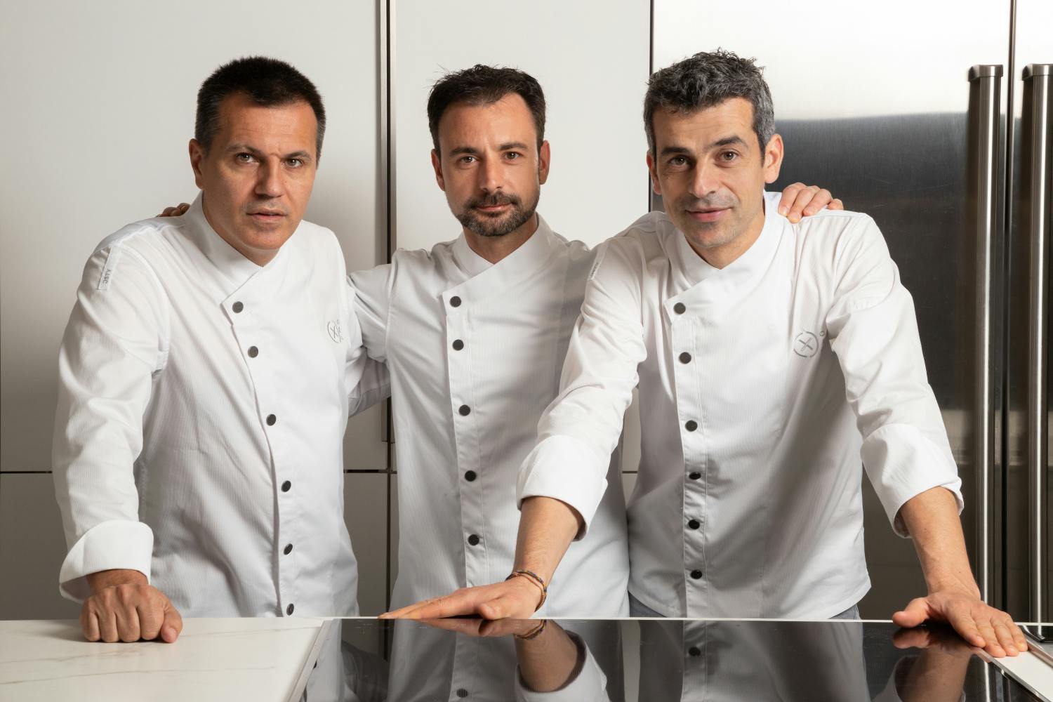 Three chefs from Disfrutar, a Three Michelin Stars restaurant, standing in front of a kitchen.