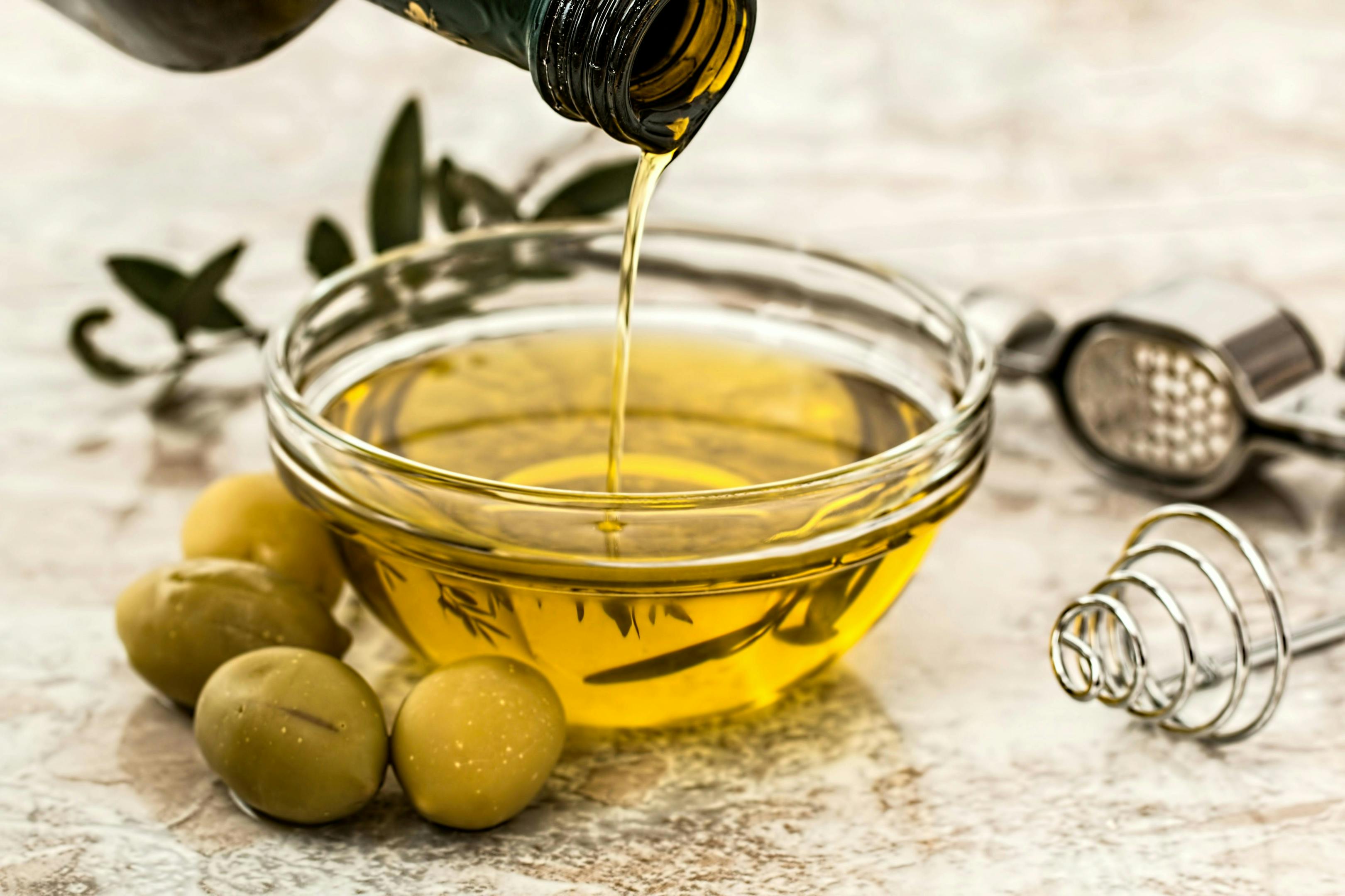 Pouring oil into a bowl next to olives.