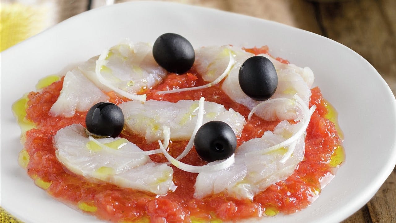 A plate of Esqueixada, a typical Catalan salad, featuring fish, olives, and tomatoes.