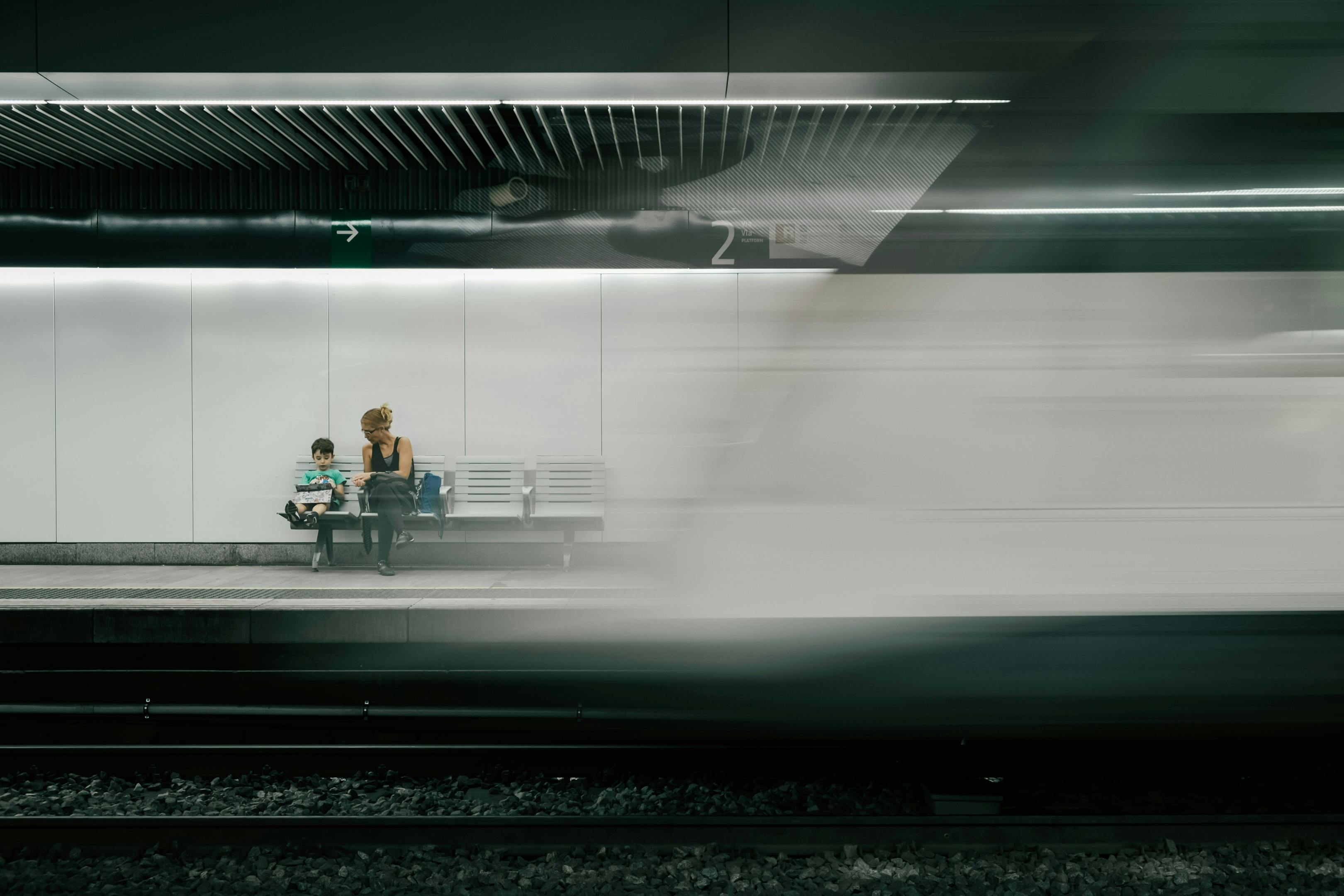 A woman seated on a bench near a train, anticipating the start of her trip.