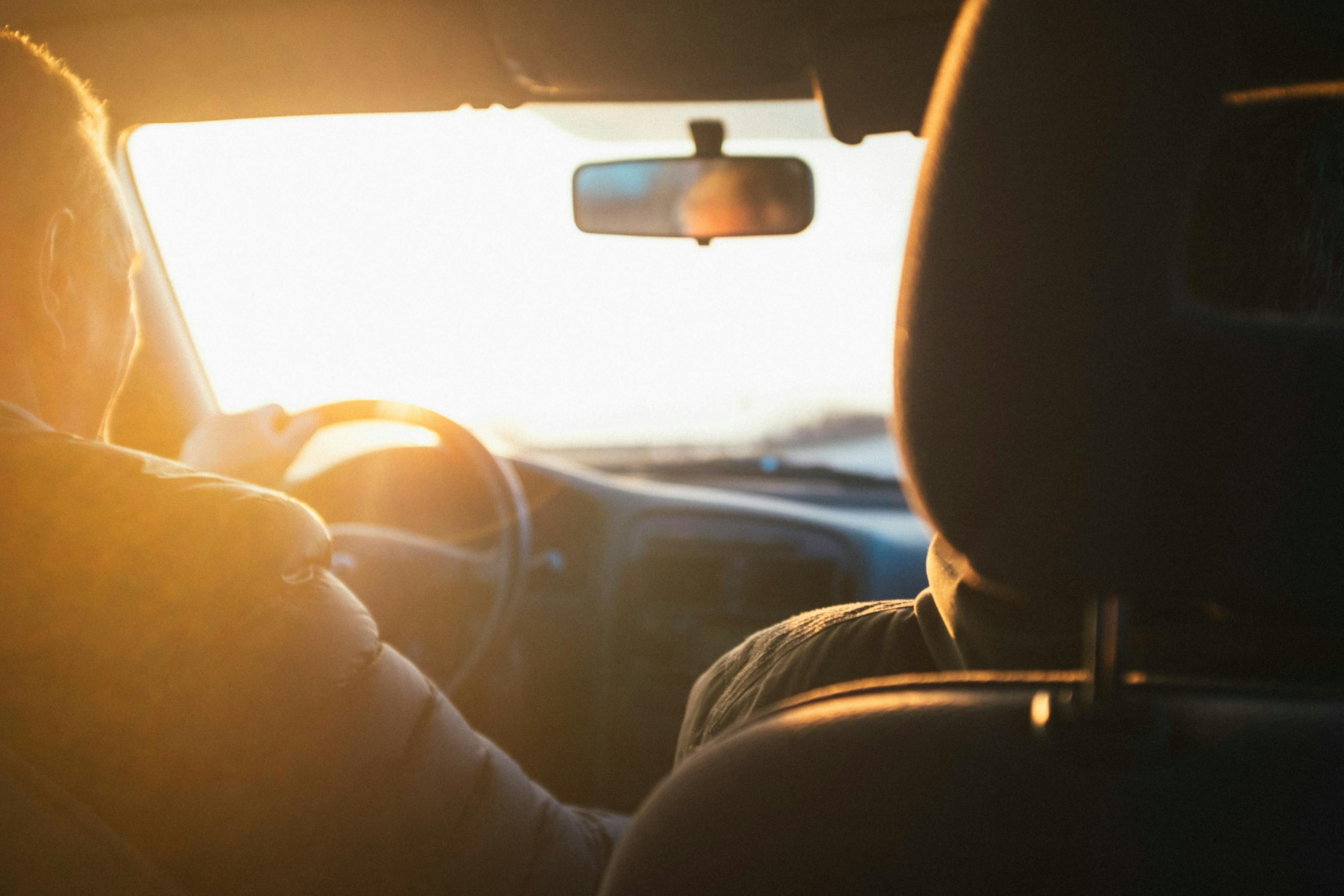 Two individuals in a vehicle driving during sunset.