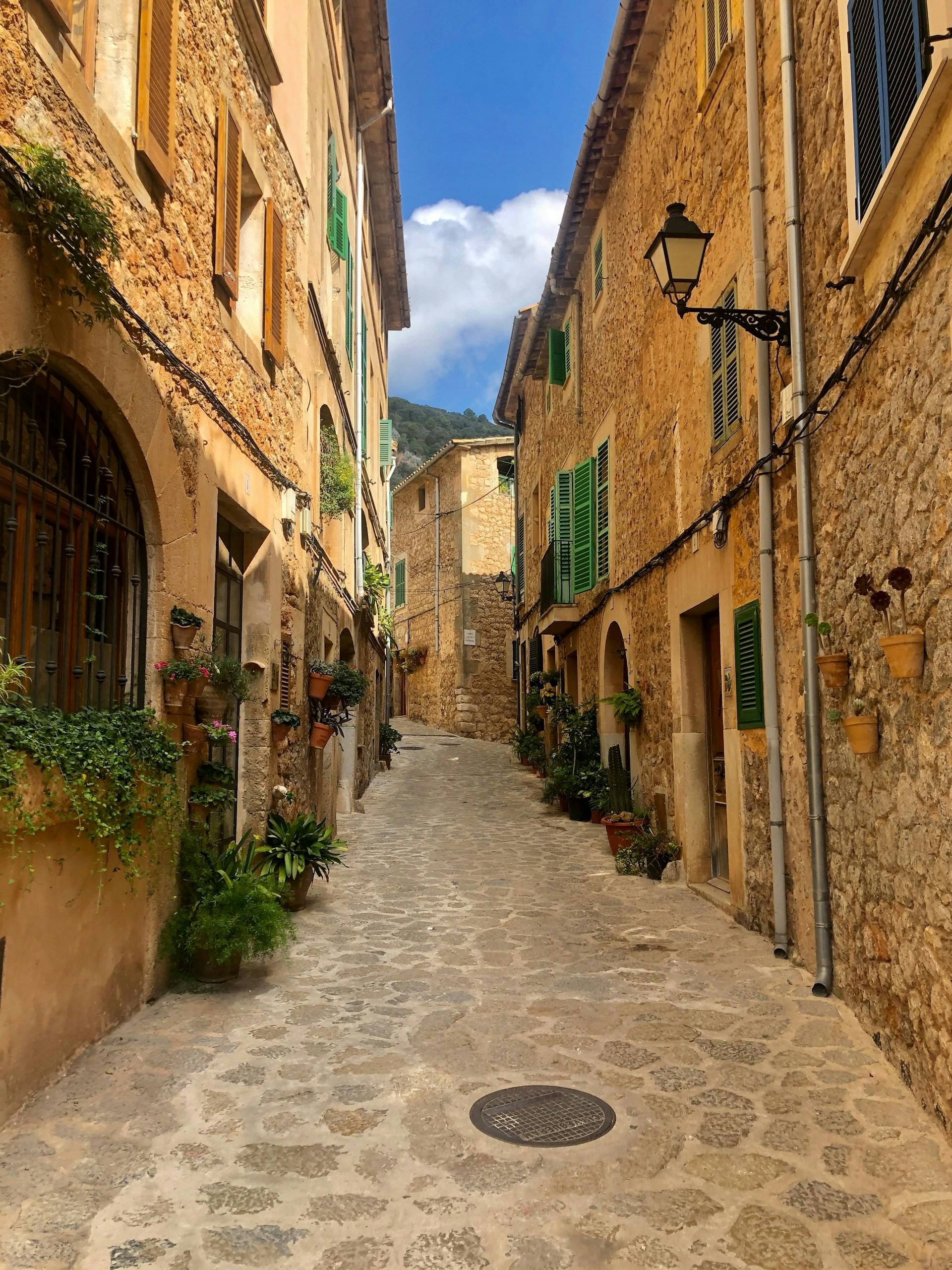 A narrow street in Valldemossa, Mallorca, lined with charming stone buildings, showcasing the village's rustic beauty.