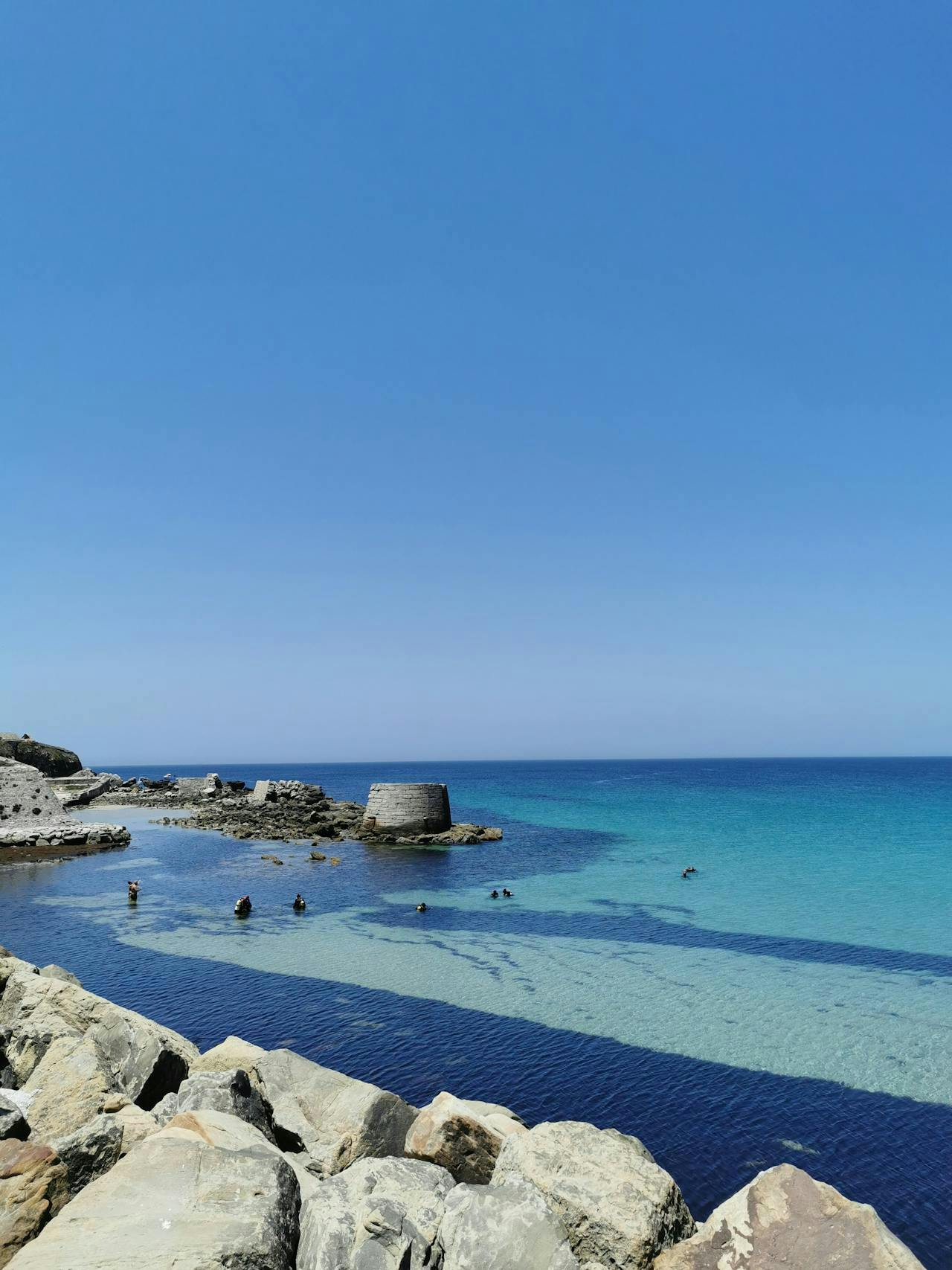 Une plage pittoresque à Tarifa avec des rochers le long du rivage et des vagues douces venant lécher le bord de l'eau.