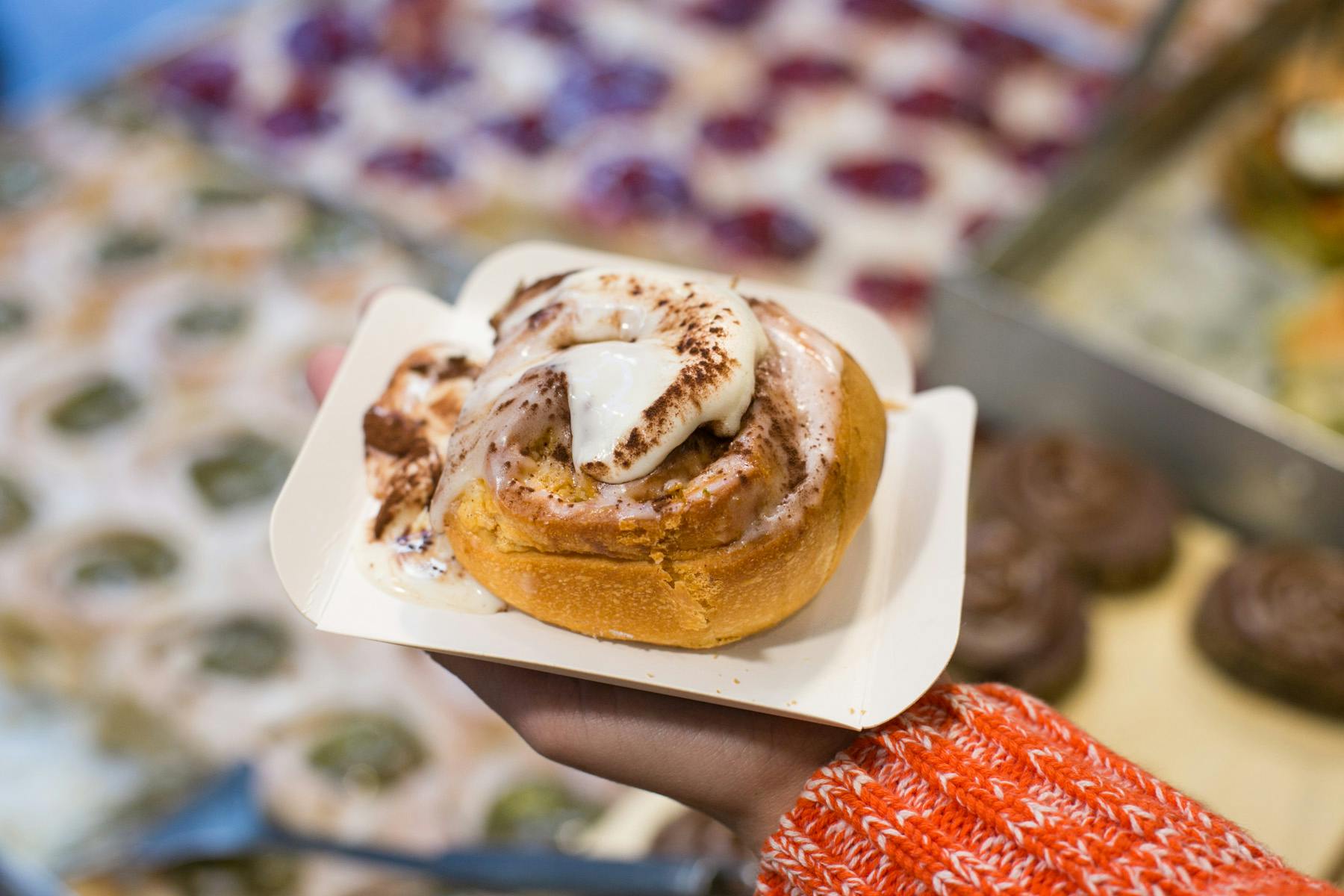 A person holding a Demasié cinnamon roll pastry.