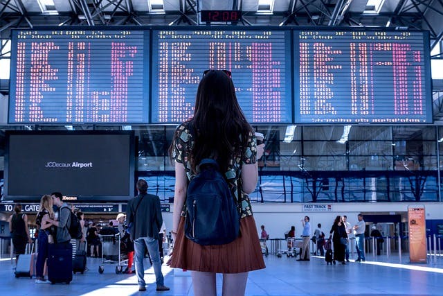 A woman stands in front of an airport terminal.