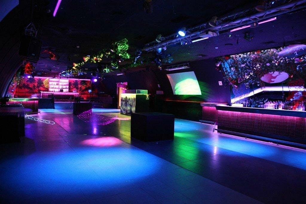 Vibrant nightclub, La Cage, featuring colorful lights and a bustling bar.