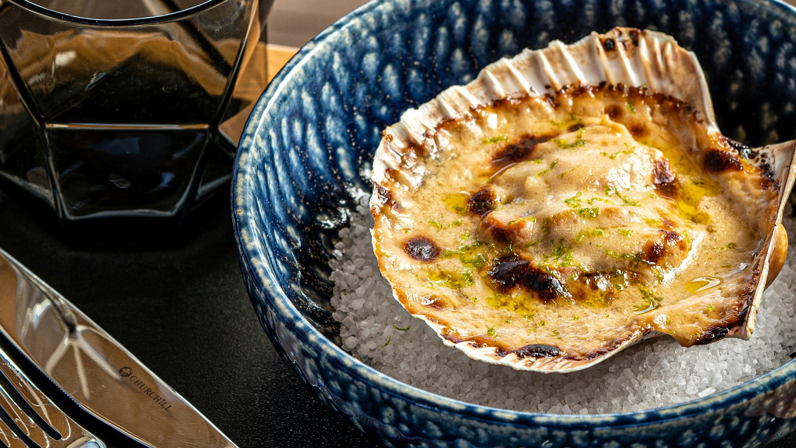 A scallop dish with a fork and knife, served in a bowl at a restaurant in Lloret de Mar.