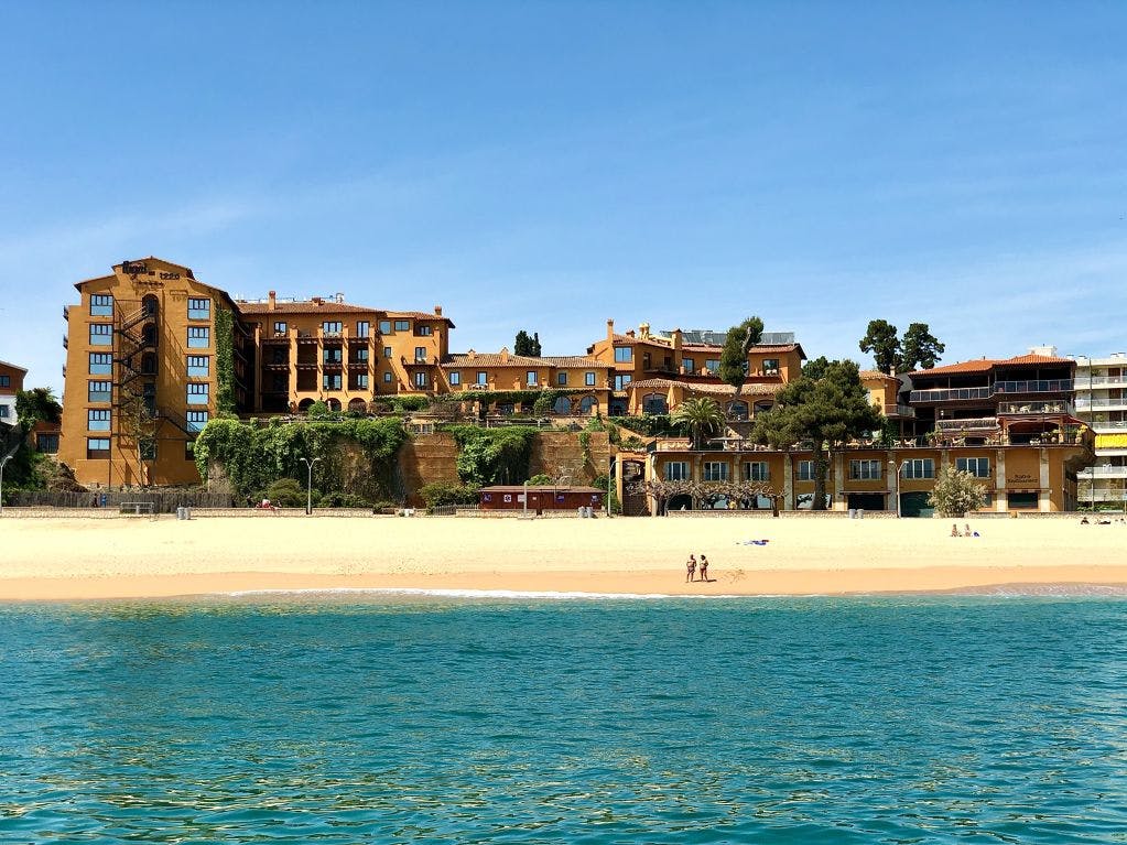 Beach with hotel on shore, palm trees, clear blue sky and calm ocean waves. 