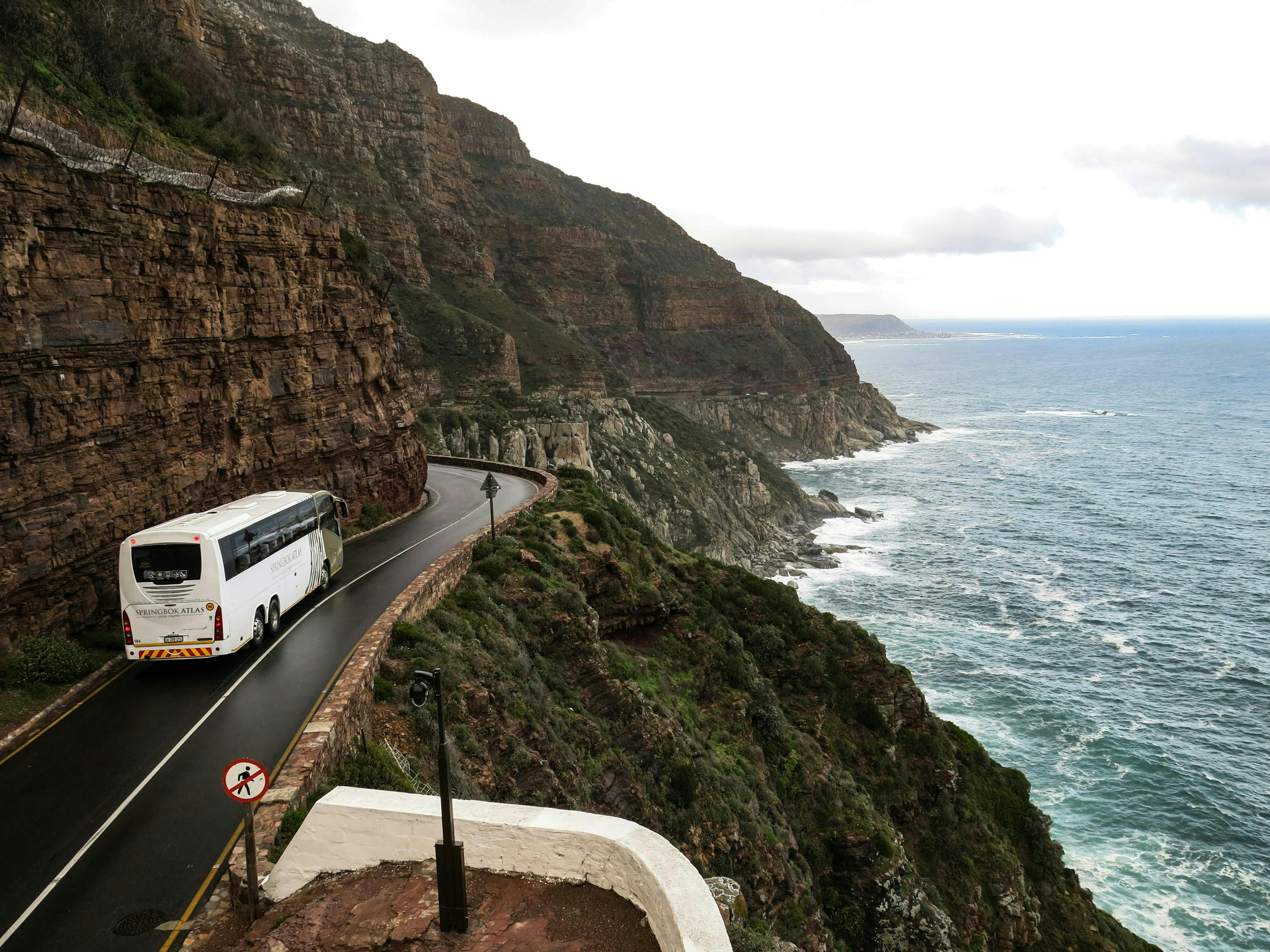 A white bus driving down a road outside the city.