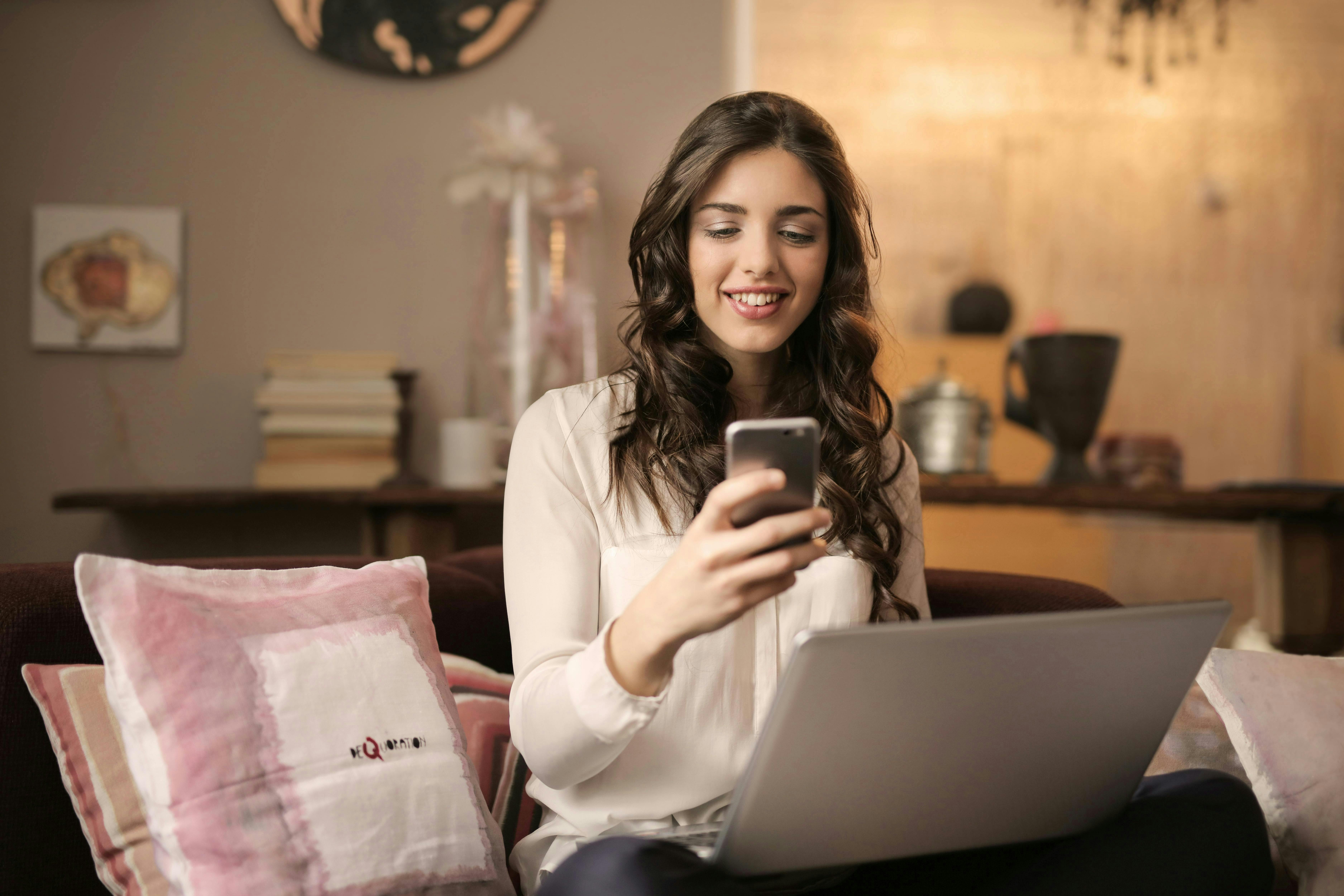 A woman sitting with a laptop and cell phone.