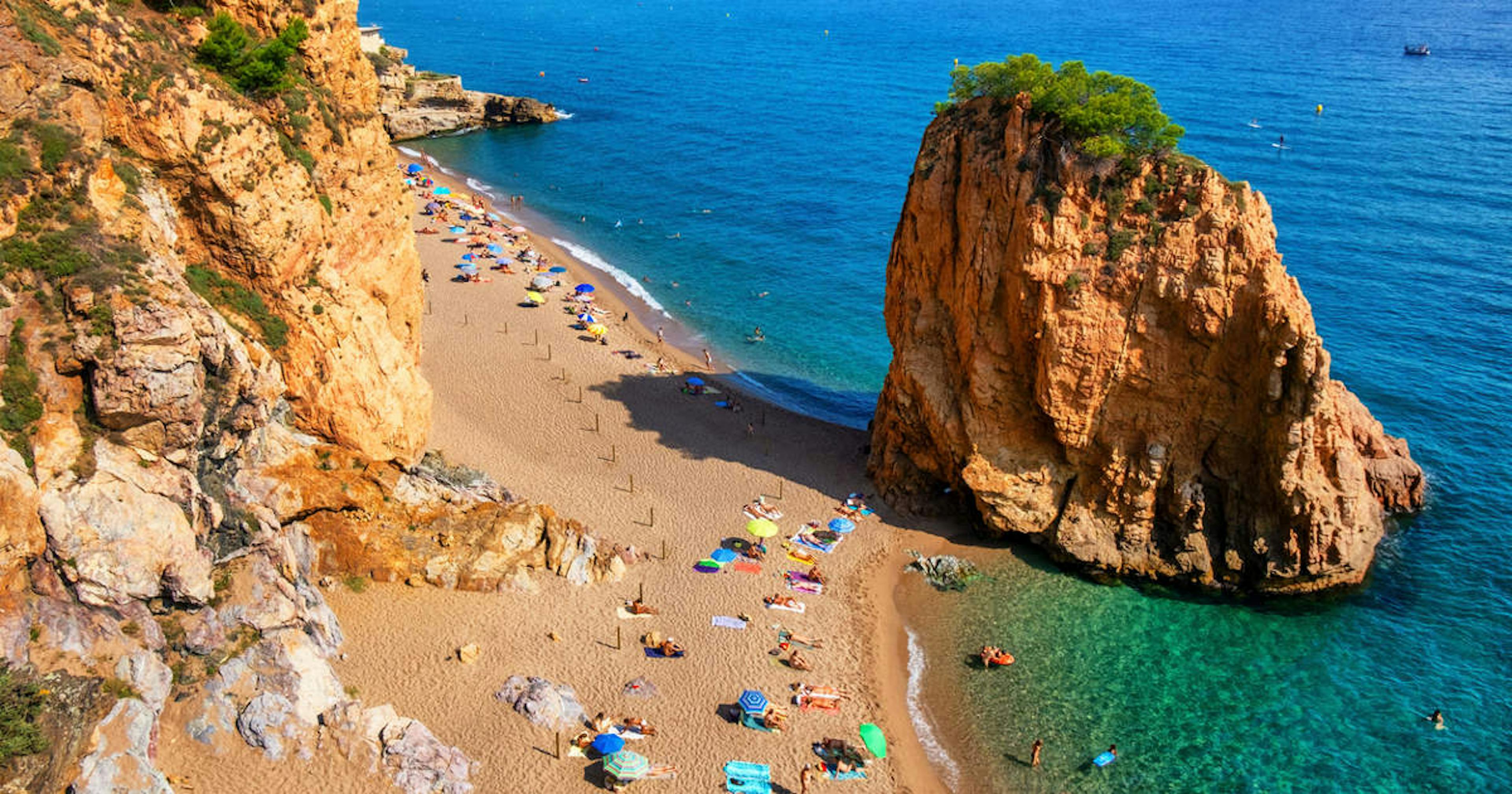 Playa de arena bajo un imponente acantilado español, que ofrece una pintoresca vista costera.