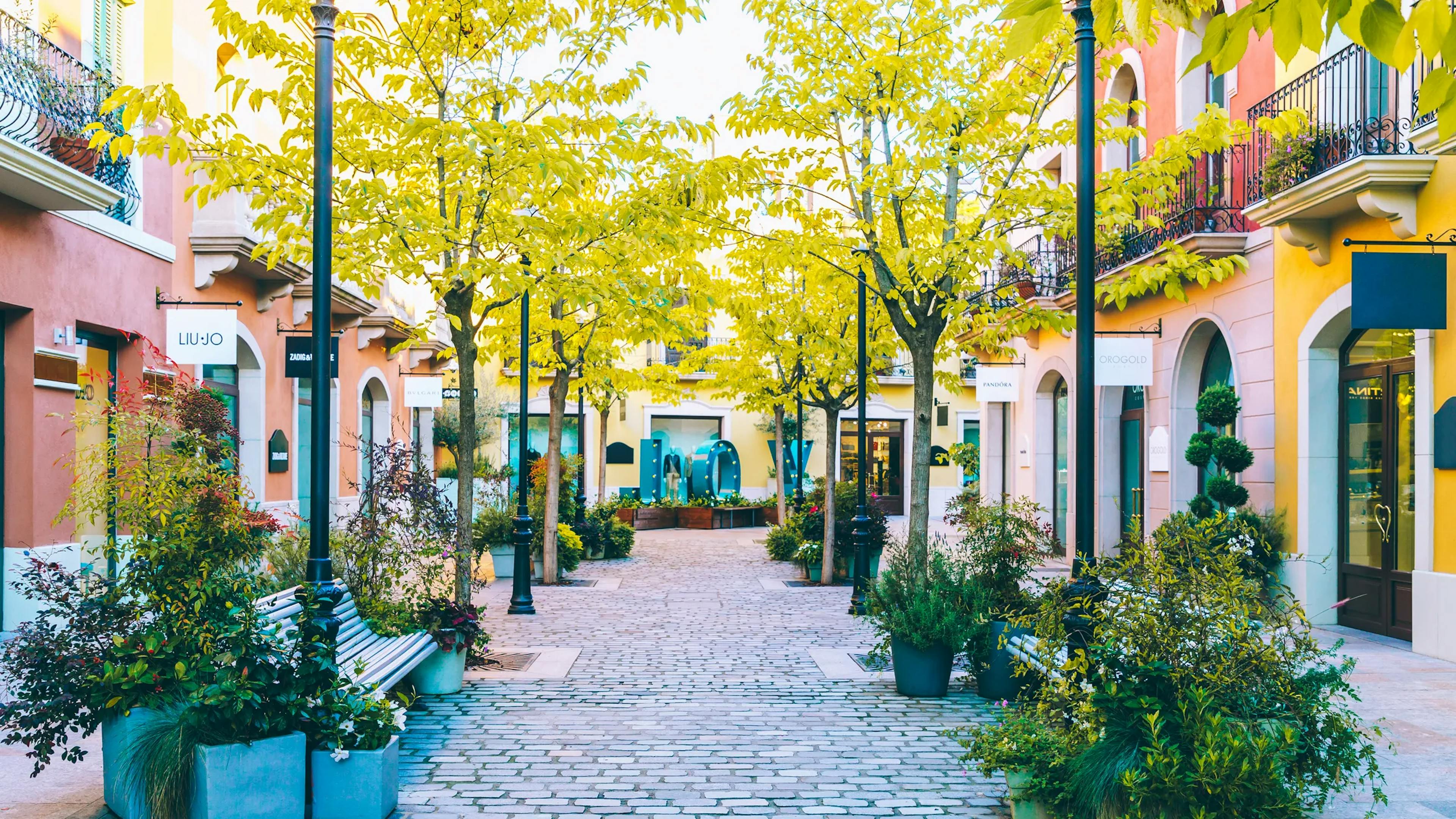 Bâtiments colorés et arbres bordant une rue étroite du centre commercial La Roca Village.