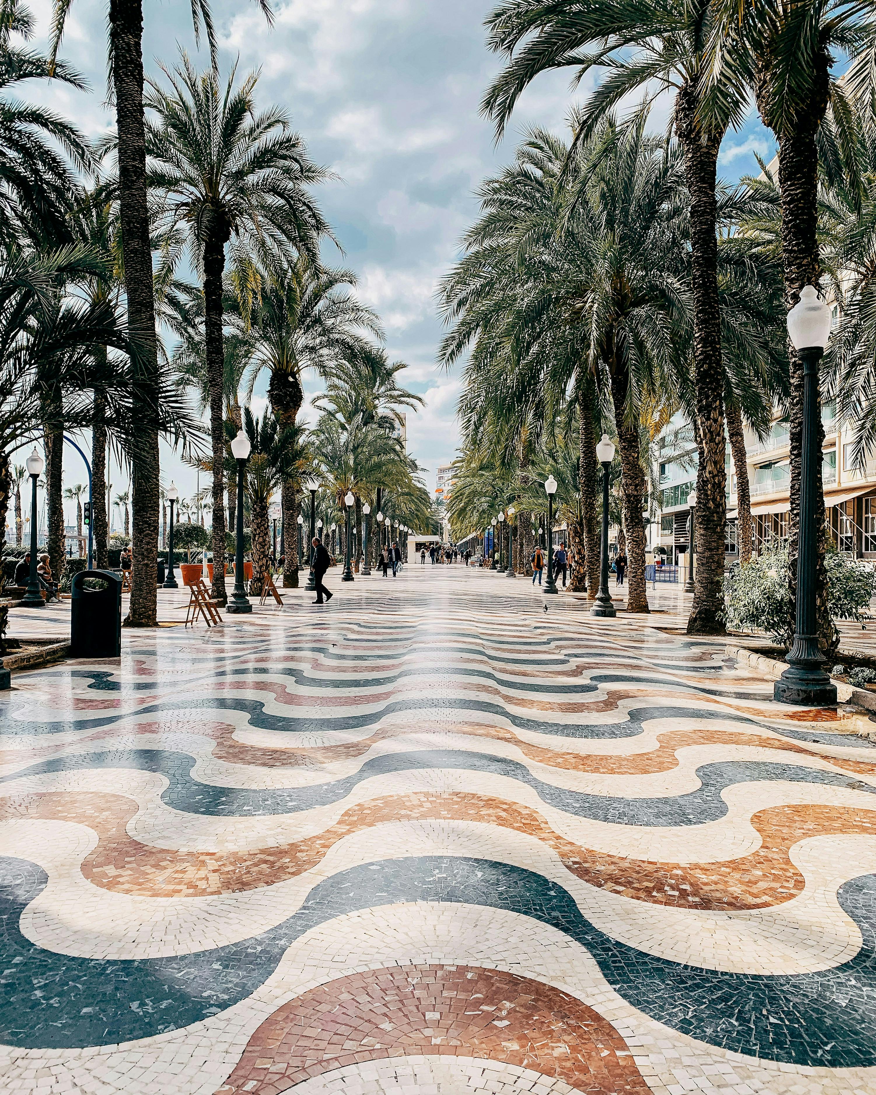 Las palmeras bordean un colorido paseo de baldosas en Alicante, creando una escena vibrante en la explanada.