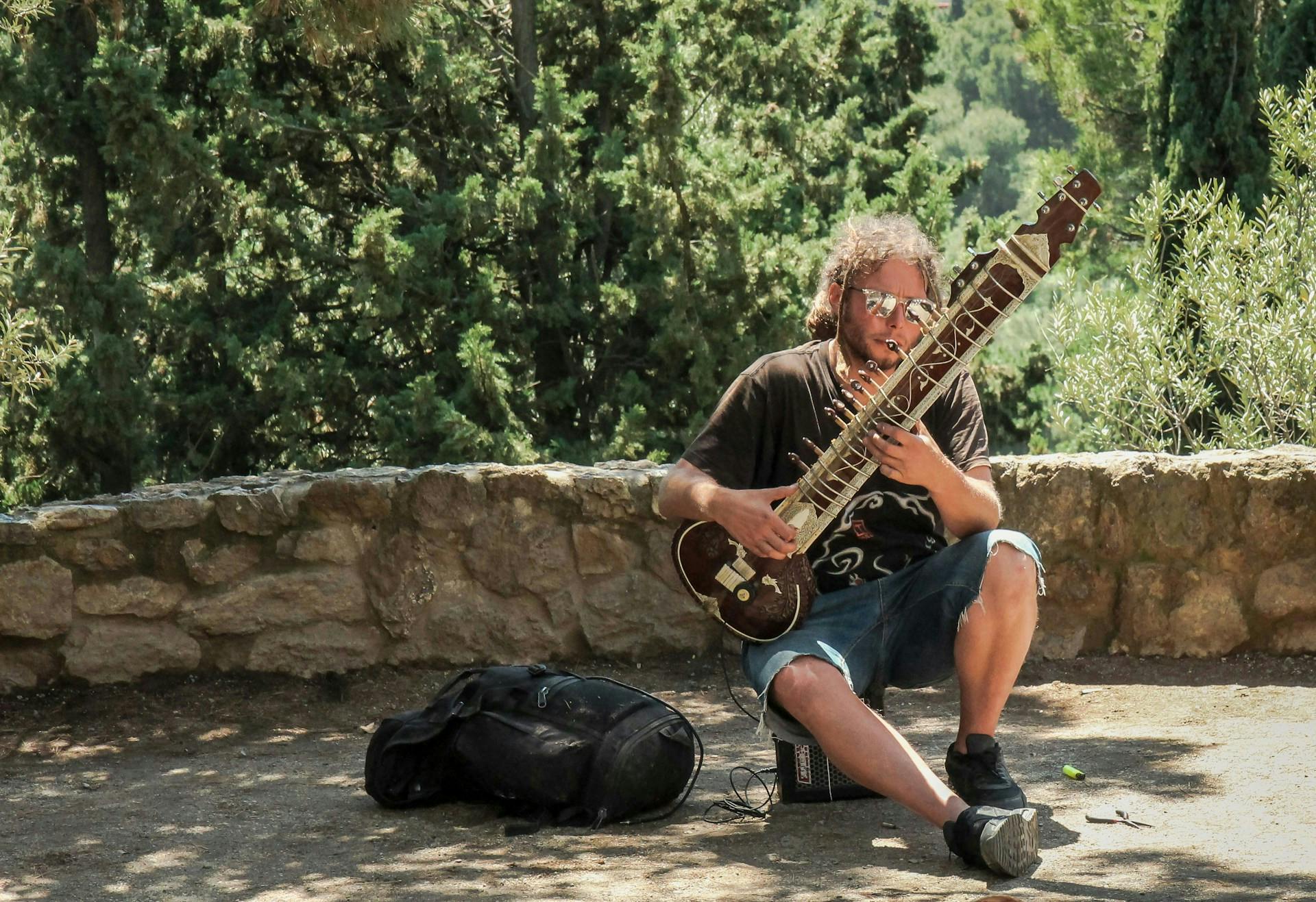 A man sits on the ground in Park Güell, Barcelona, playing a musical instrument with a serene expression.