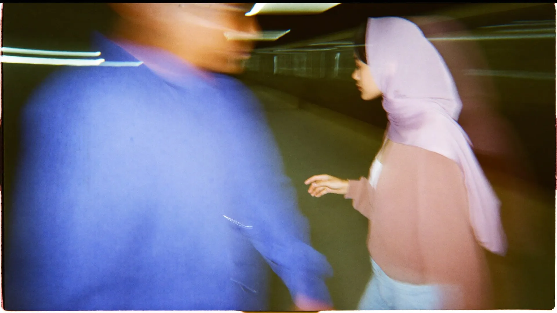 Two young Egyptians crossing in opposite directions on a Cairo metro platform at night, blurred into streaks.