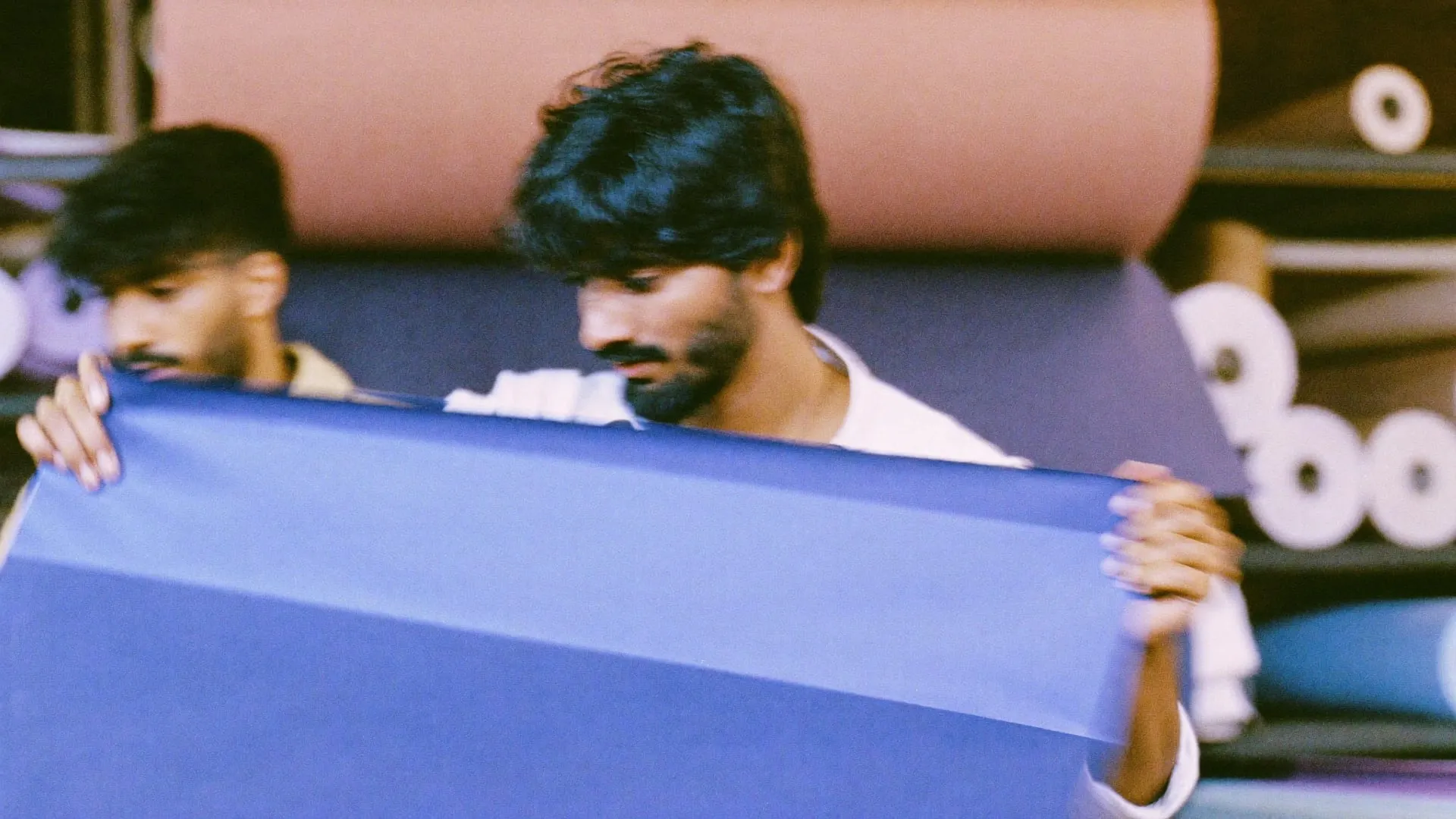 A man pulling a large sheet of periwinkle paper from a roll in a workshop