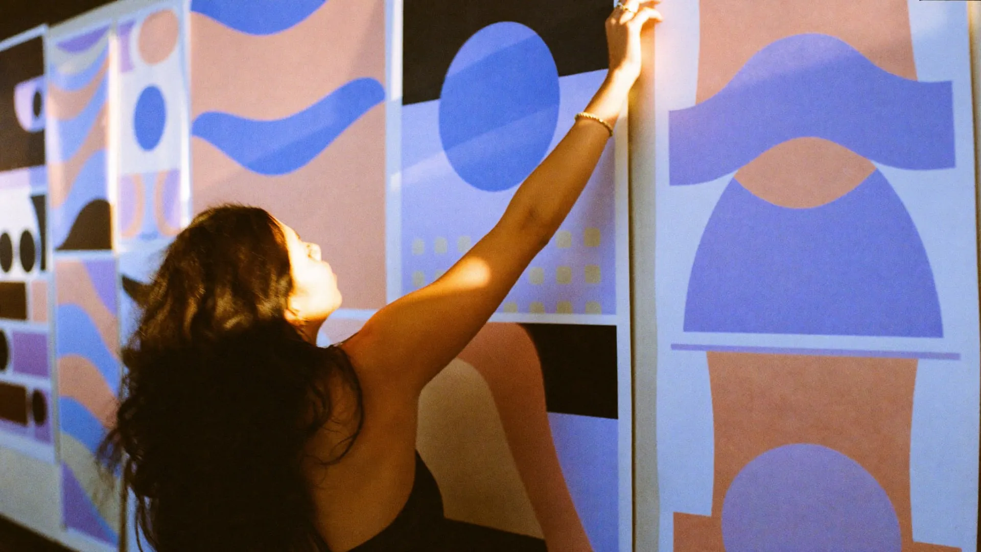 A designer pinning large colour swatch sheets onto a tall studio wall in afternoon light
