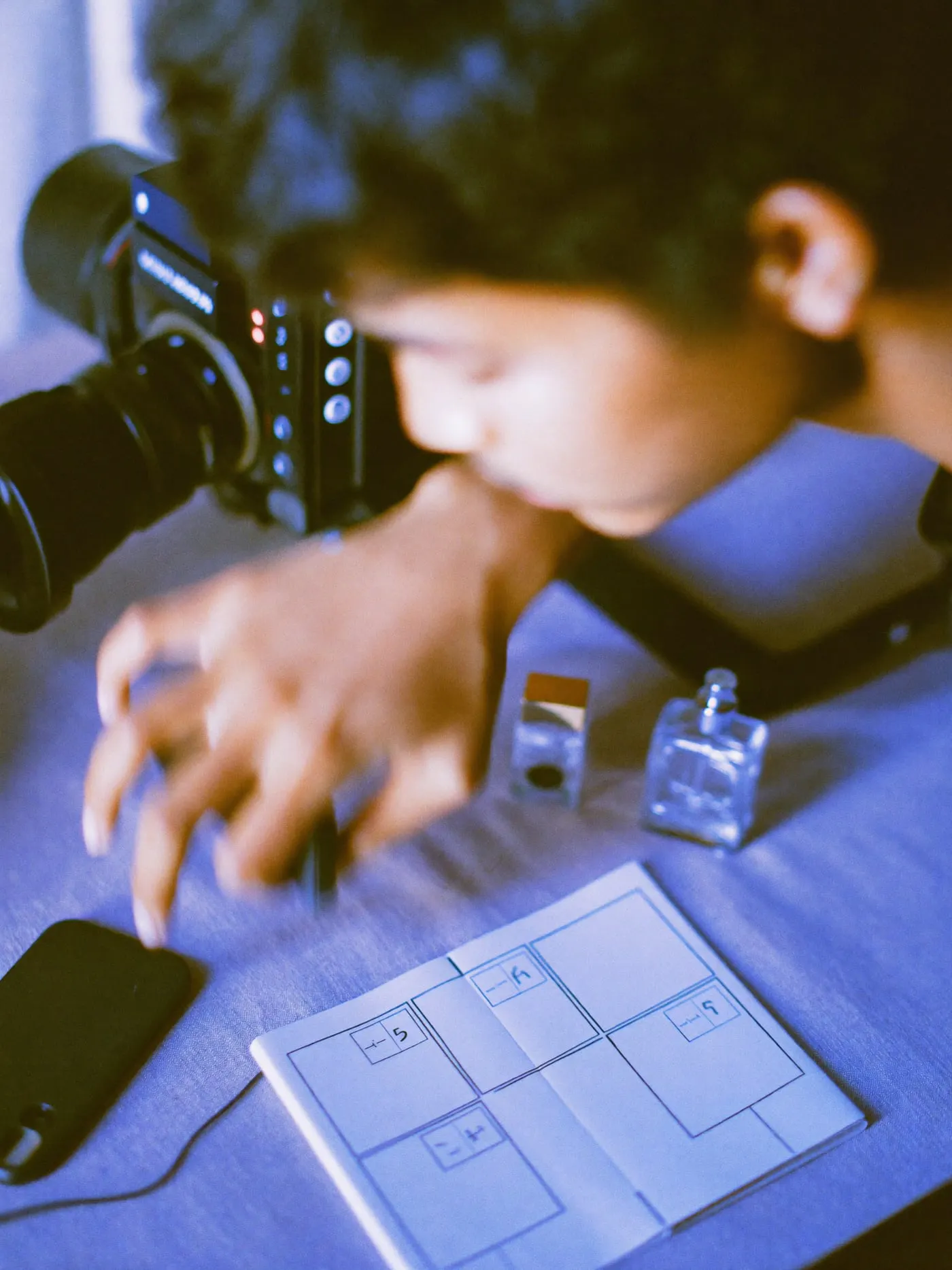 A hand reaching for a gimbal on a table with a camera, phone and small product