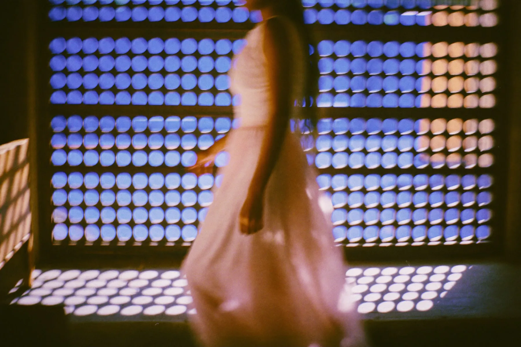 Sunlight through a carved wooden lattice throwing a grid of light across a woman walking past