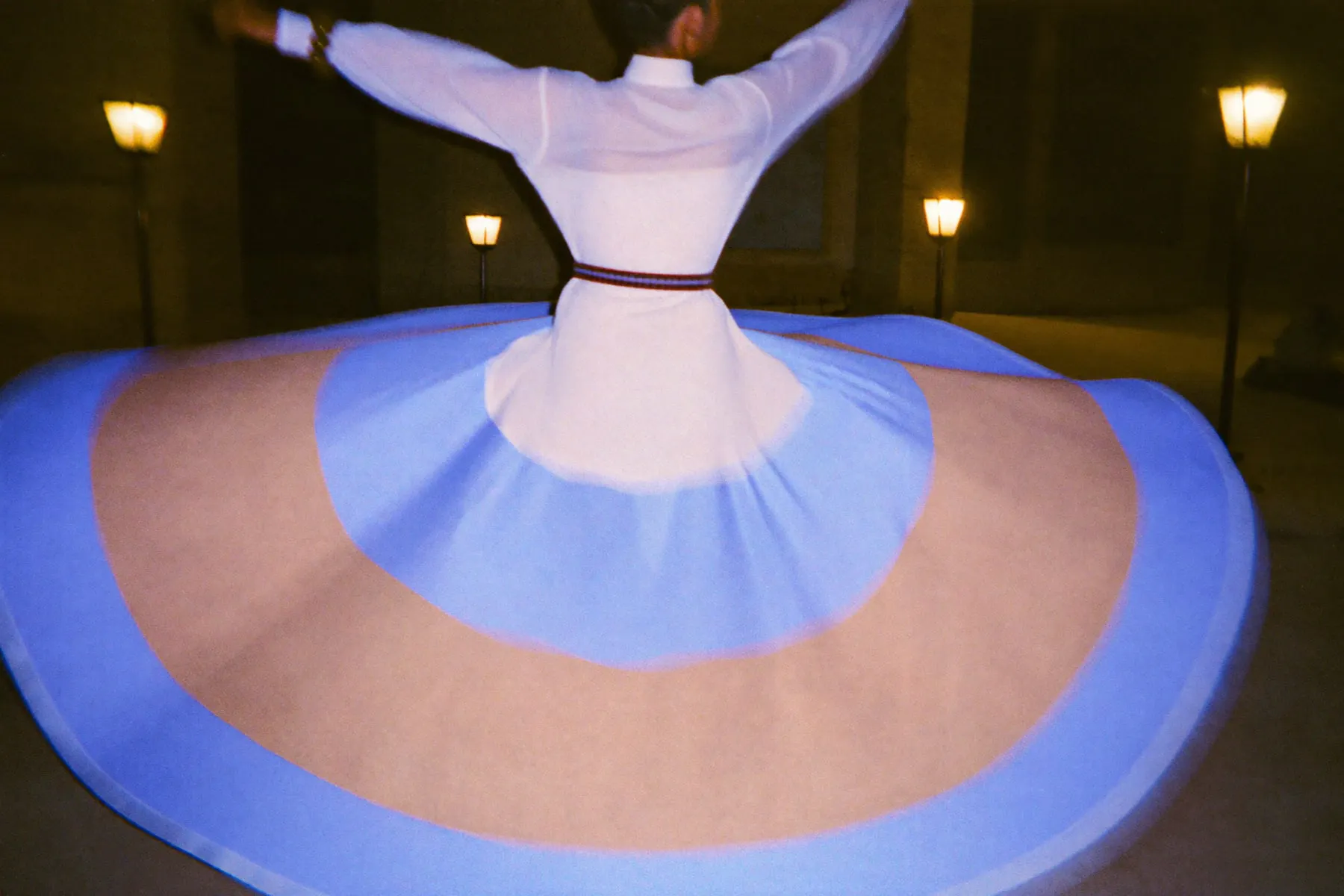 A tanoura dancer spinning in a dim Cairo courtyard, the skirt smeared into a disc of colour