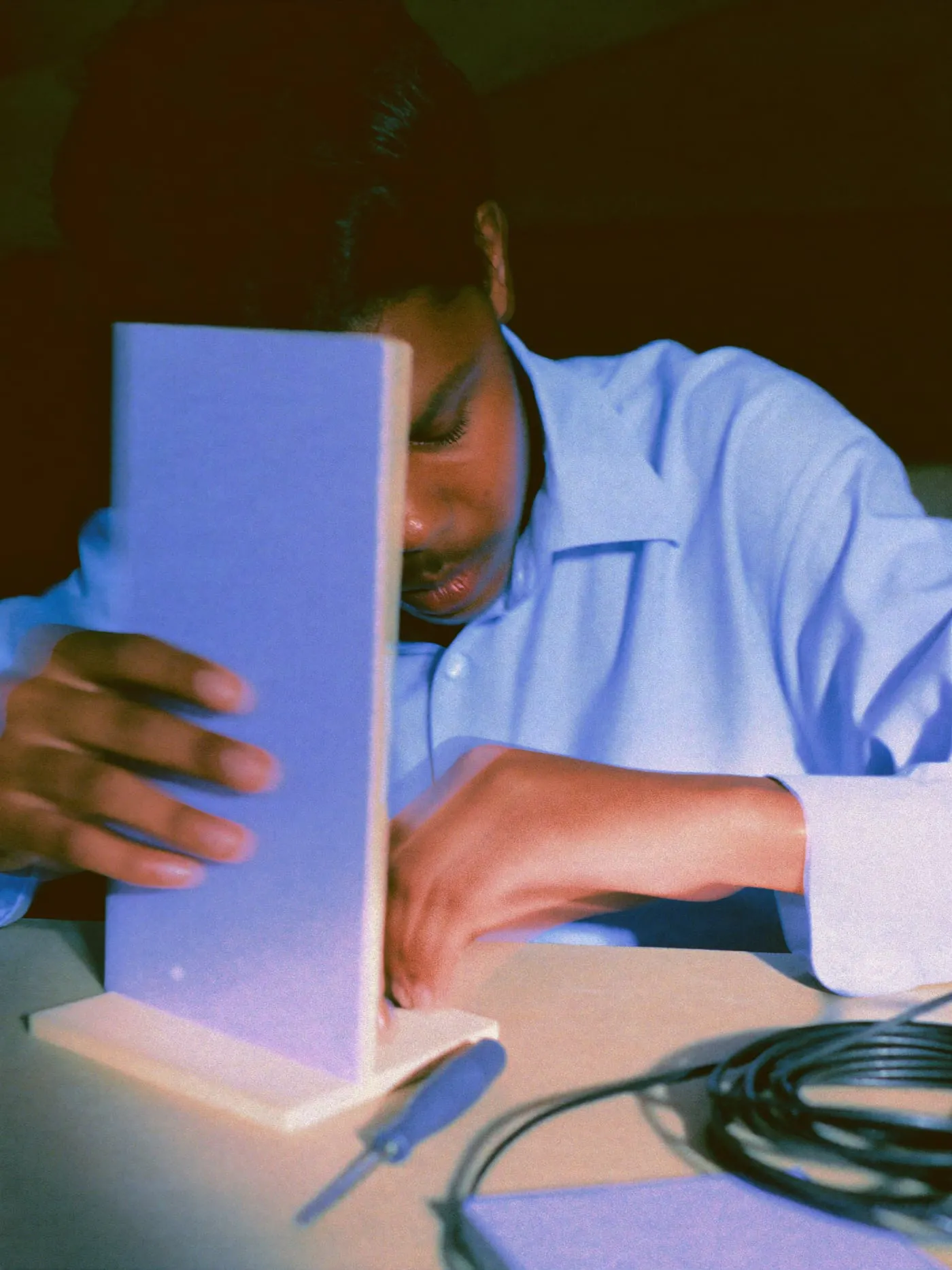 Hands assembling a plywood phone stand beside a cable and a screwdriver