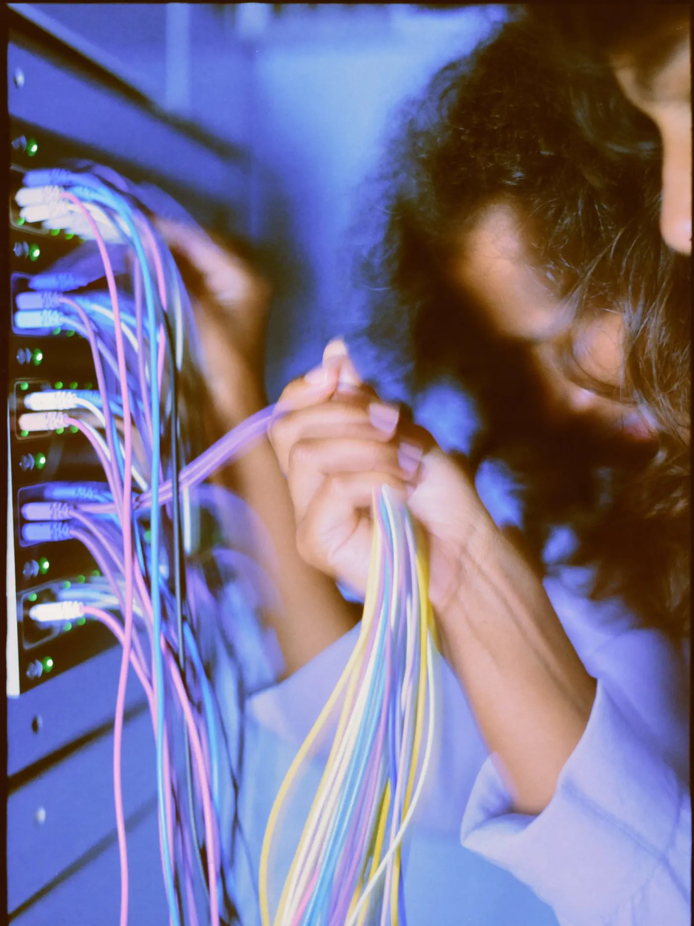 Hands plugging colour coded network cables into a patch panel in a rack