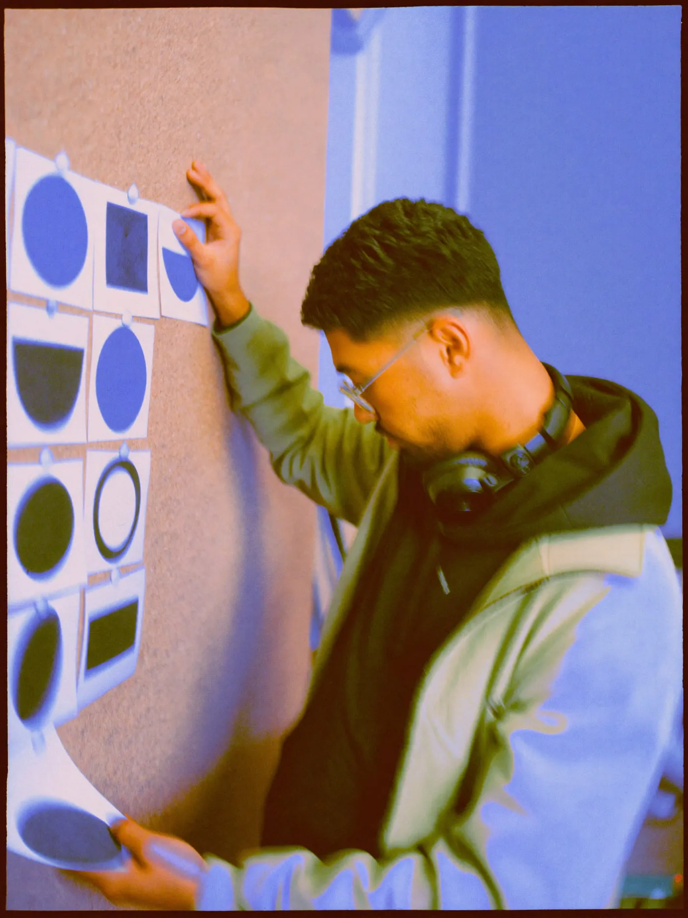 A designer pinning a grid of simple circle and ring shapes on a cork wall to compare them