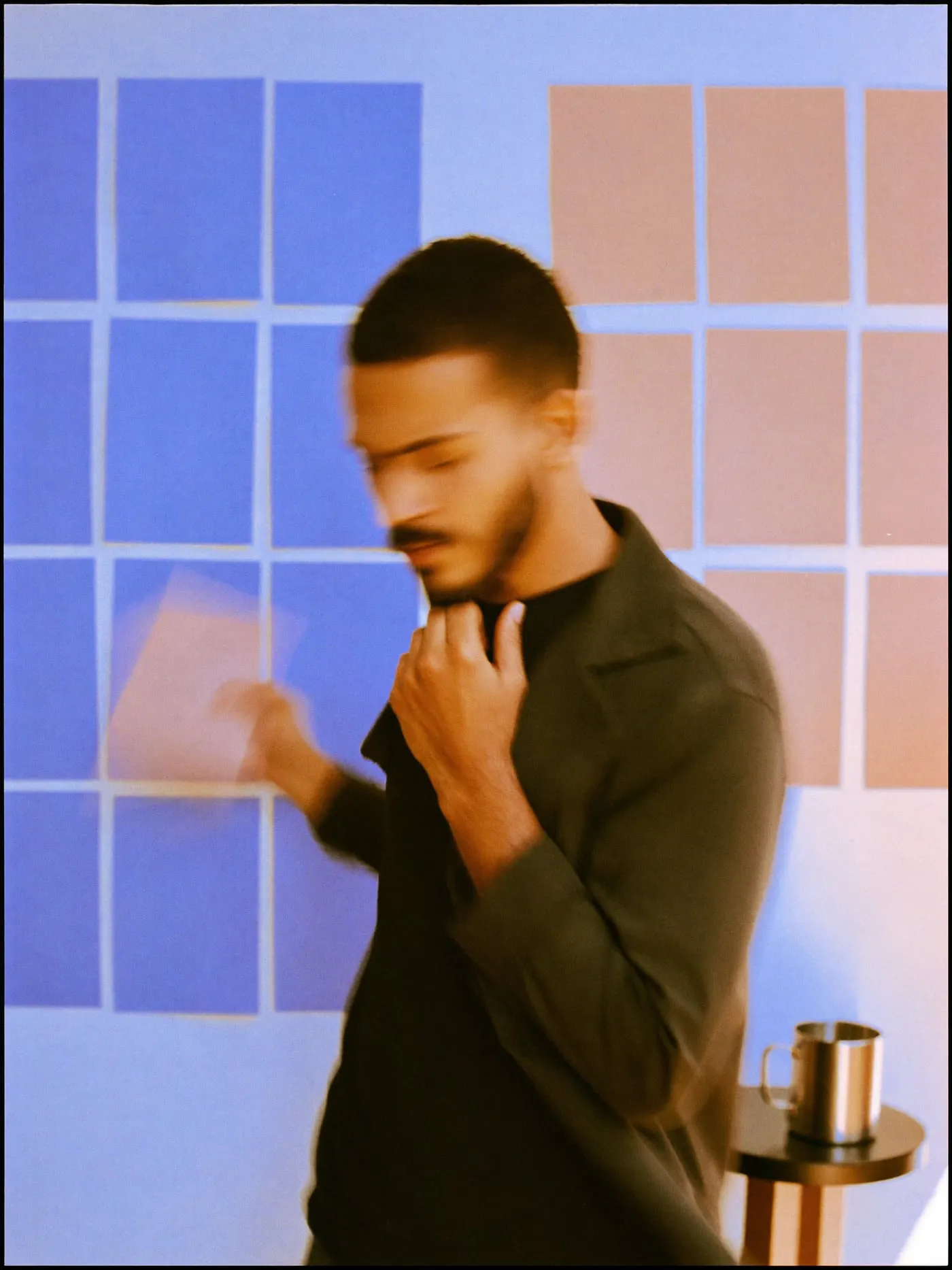 A bearded man in a charcoal jacket weighing two groups of blank cards on a studio wall