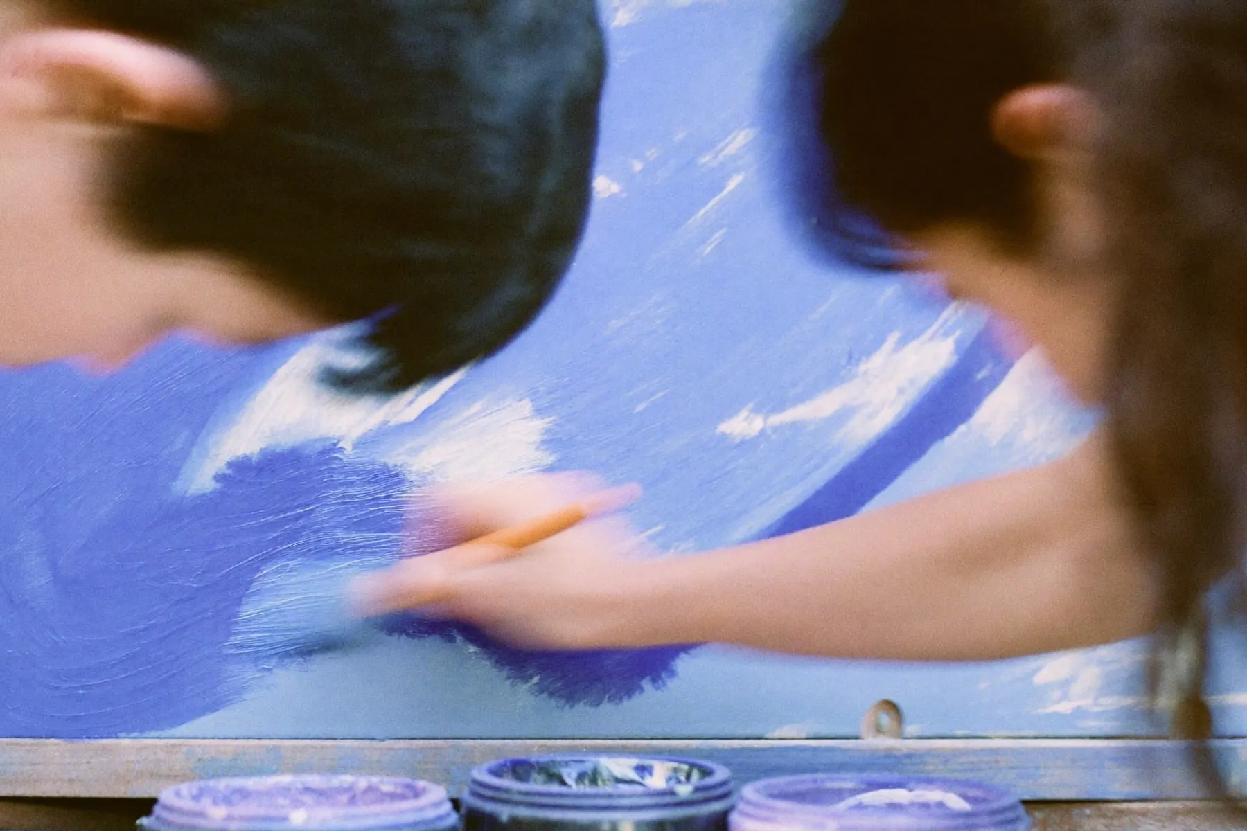A hand painting a faded wooden panel with a fresh coat of saturated blue