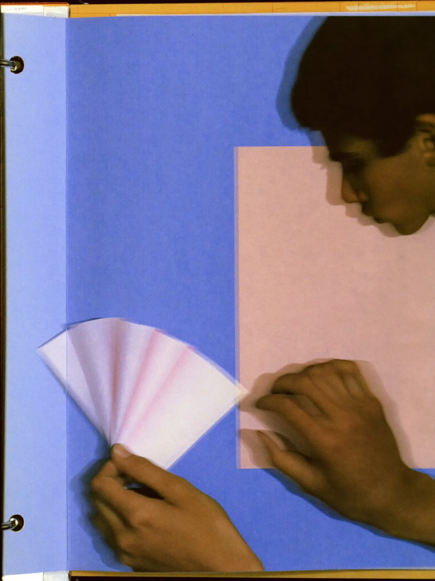 Two hands reaching for the same page of an open binder of colour blocks