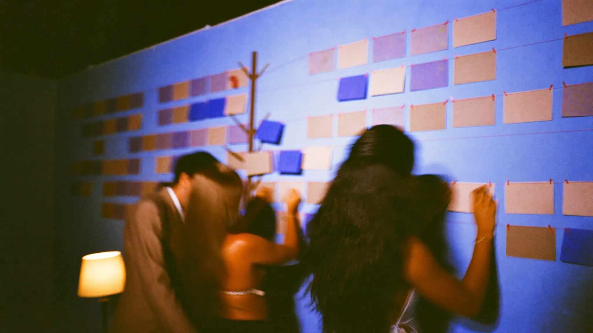 Two people rearranging rows of blank cards joined by thread on a long studio wall