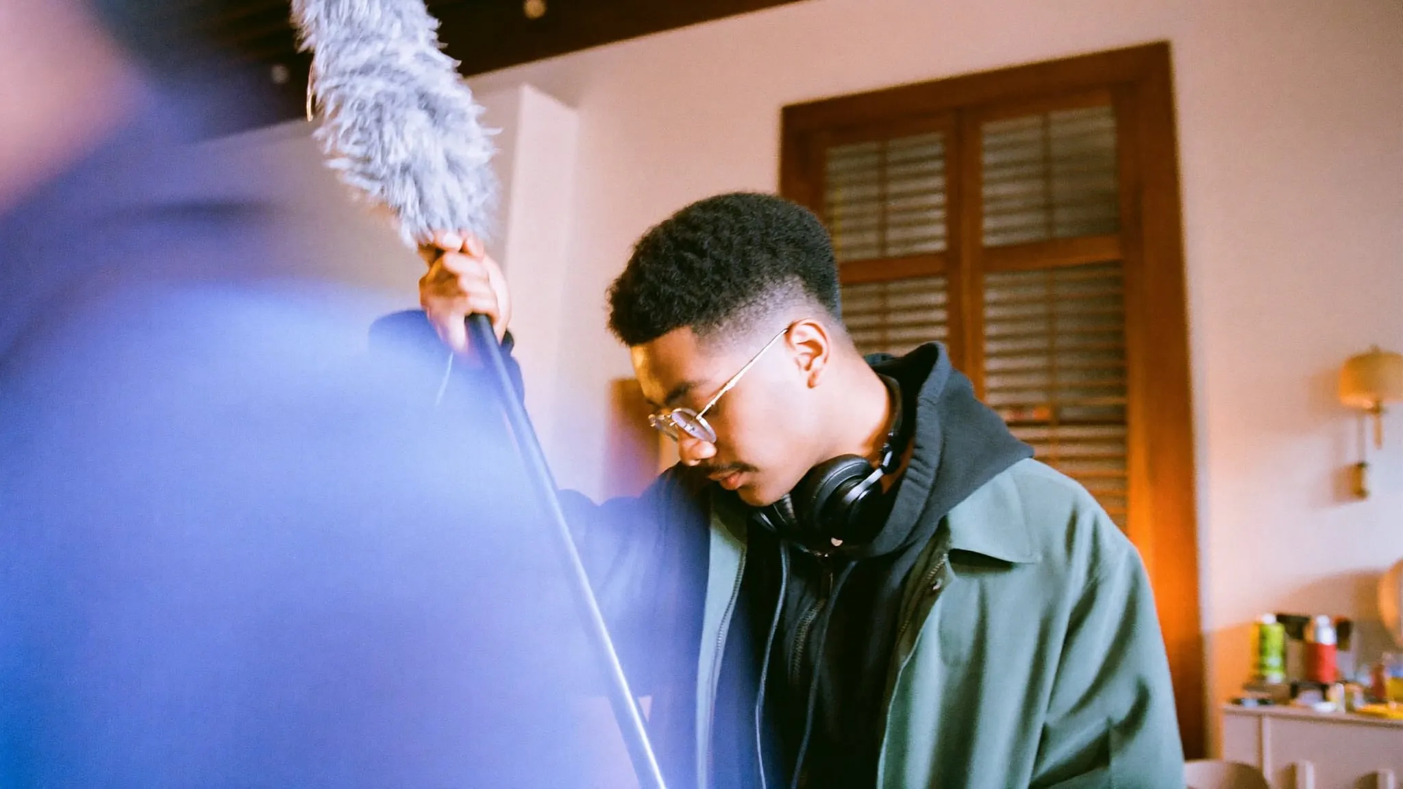 A young man in glasses raising a boom microphone on a pole inside an old downtown Cairo apartment