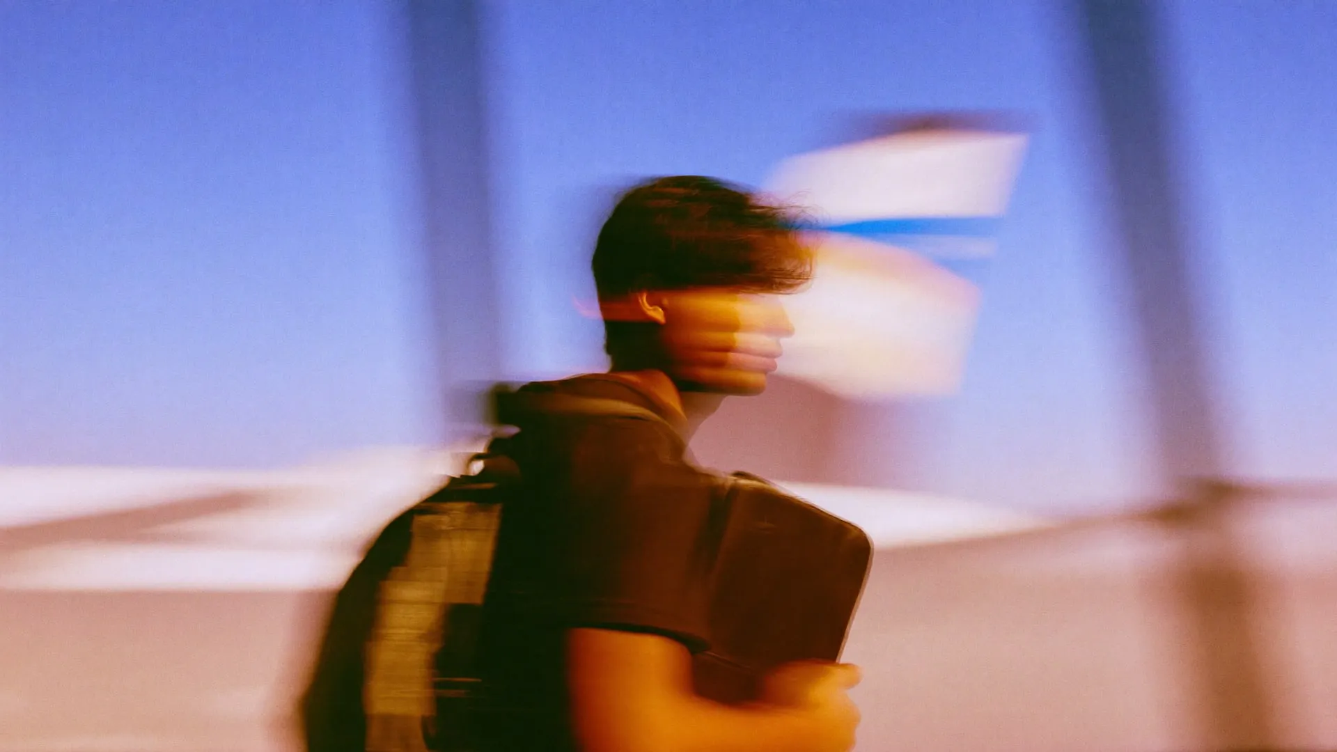 A young man walking past airport windows at dawn with a portfolio case under his arm